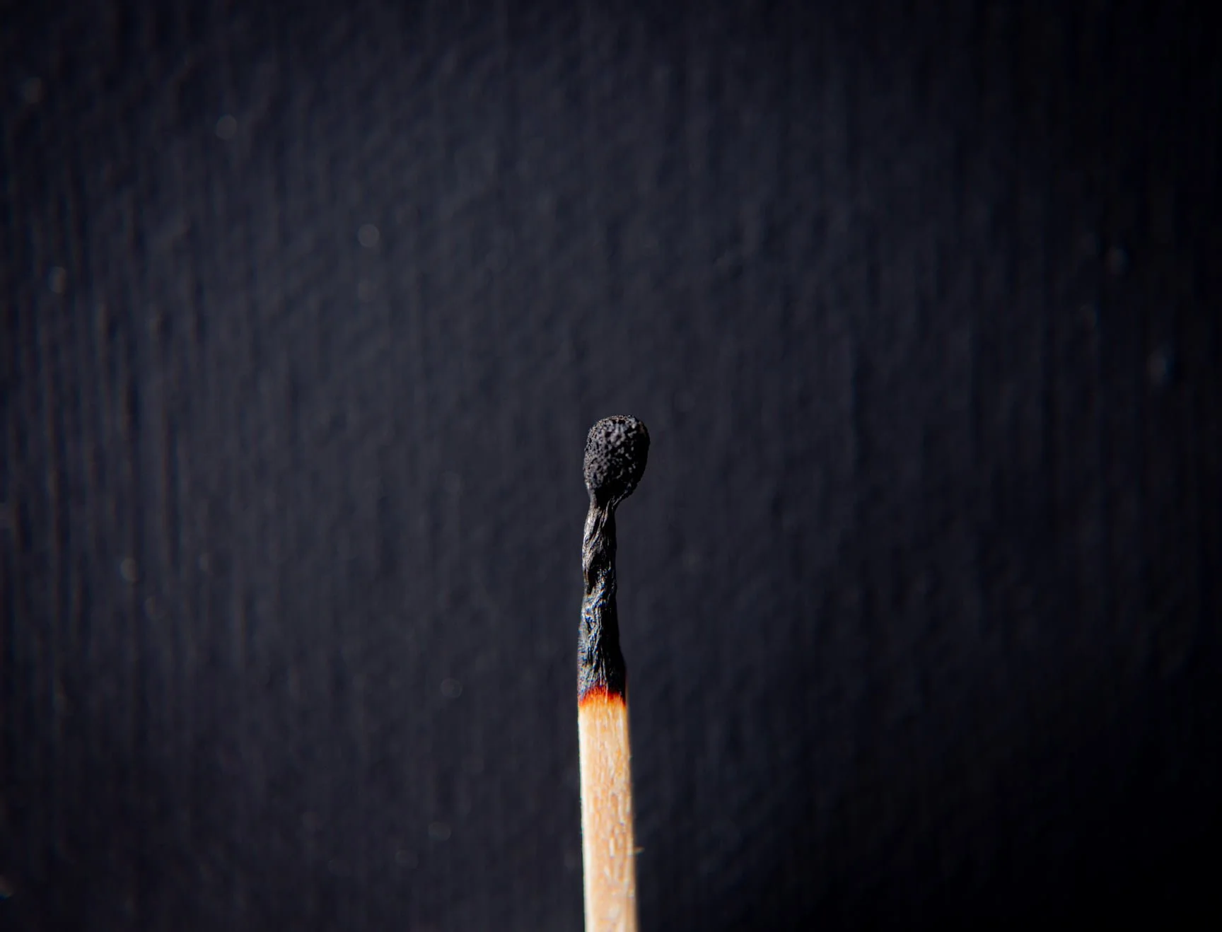 Close-up view of a burnt wooden matchstick with a blackened head against a dark background.