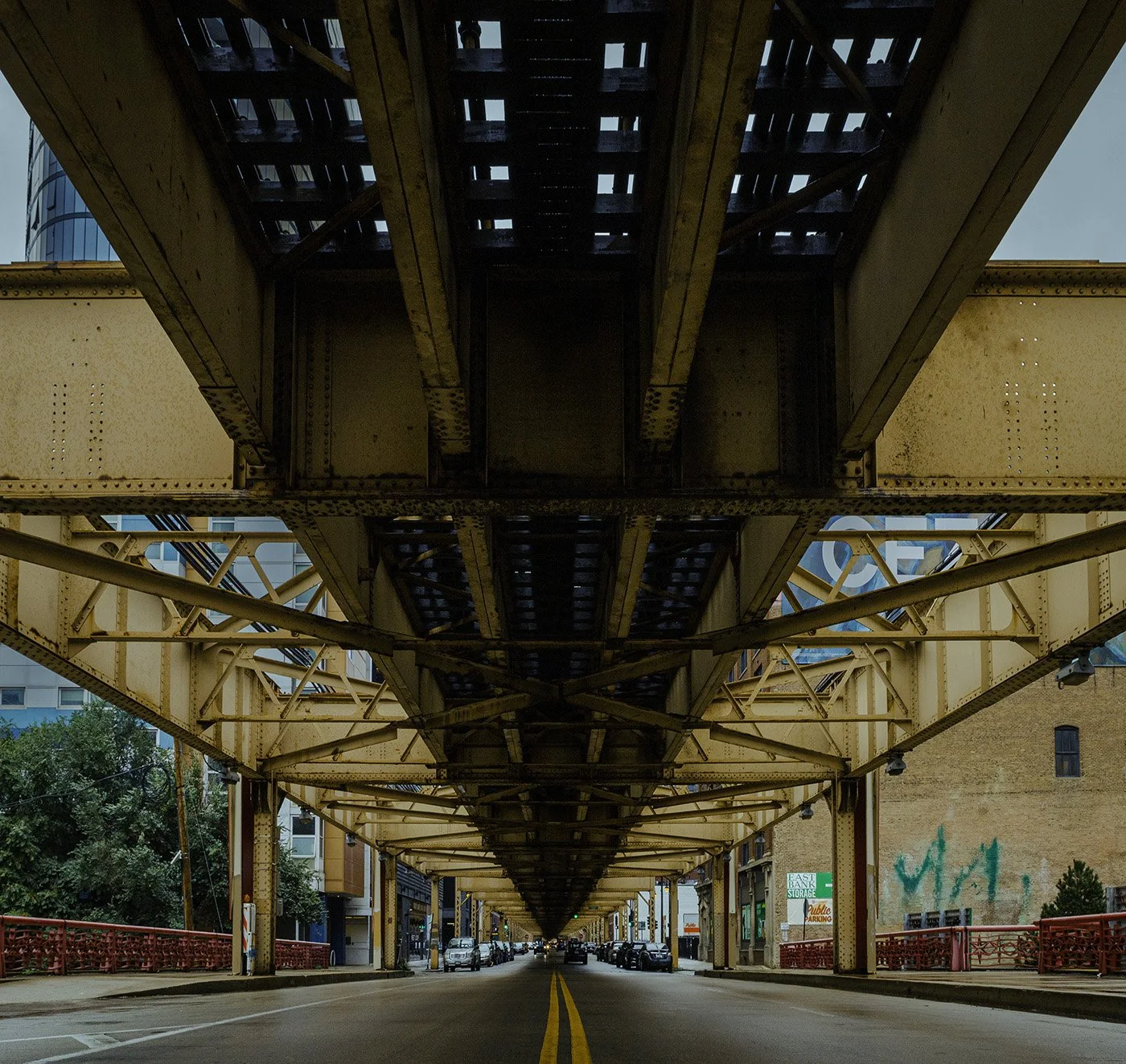 Underground train track structure above city street with parked cars and building facades.