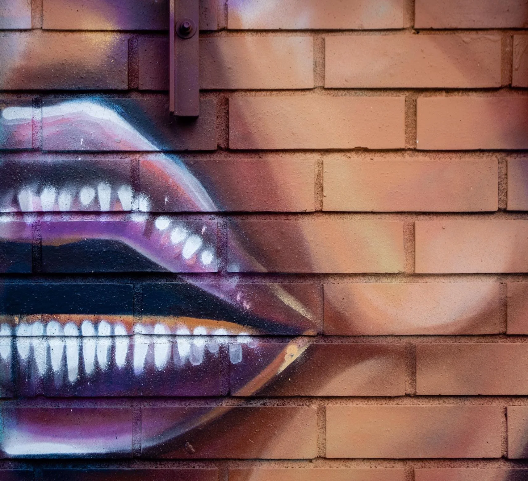 Close-up of graffiti art on a brick wall depicting an open mouth with teeth, painted in vibrant colors.