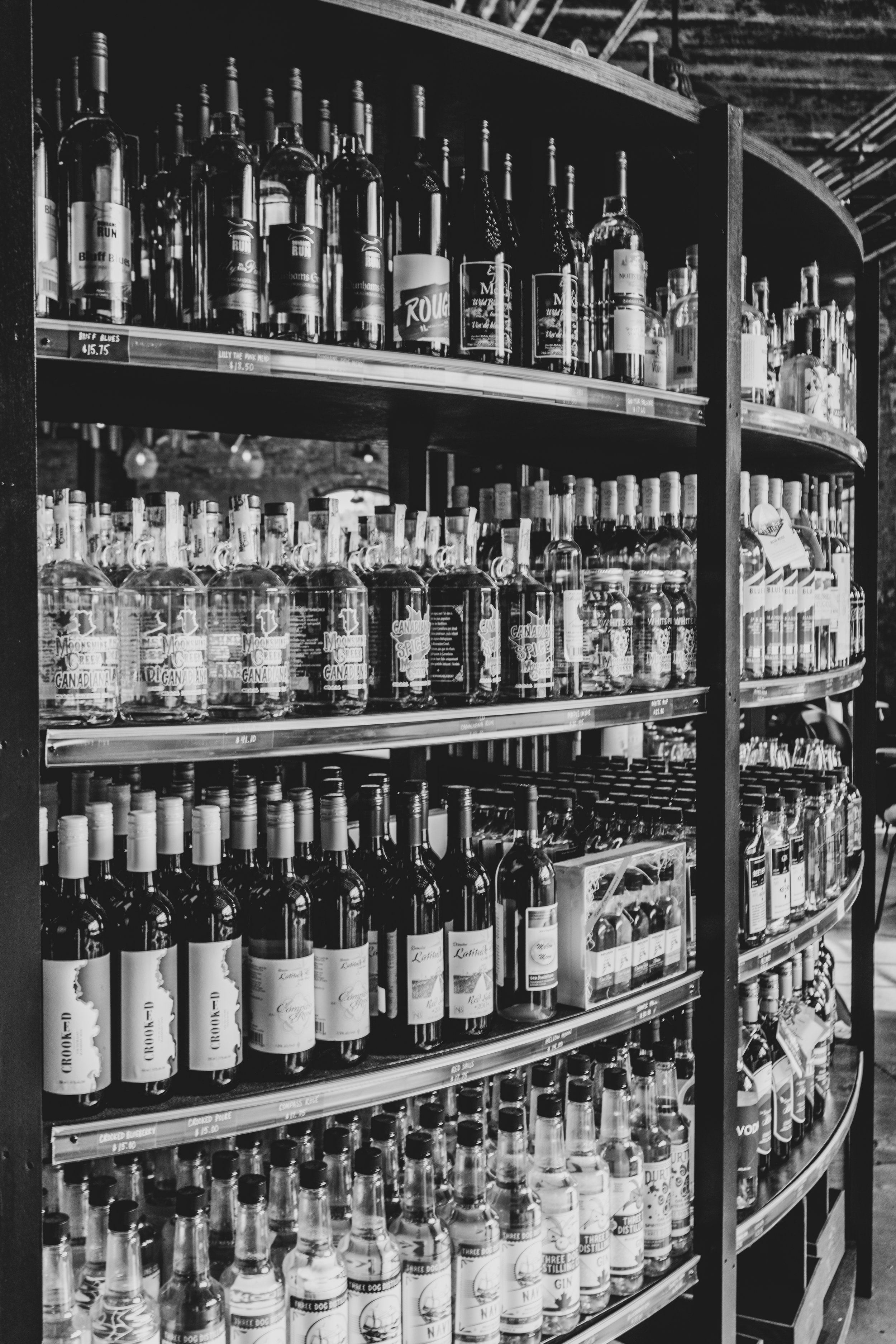 Black and white photo of metal shelves filled with various types of liquor bottles in a store.