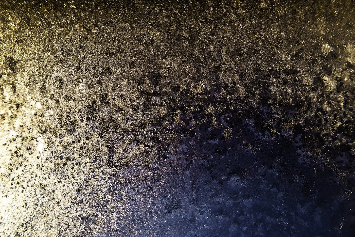 Close-up of a textured surface with dark specks, a frozen surface with frost deposits.