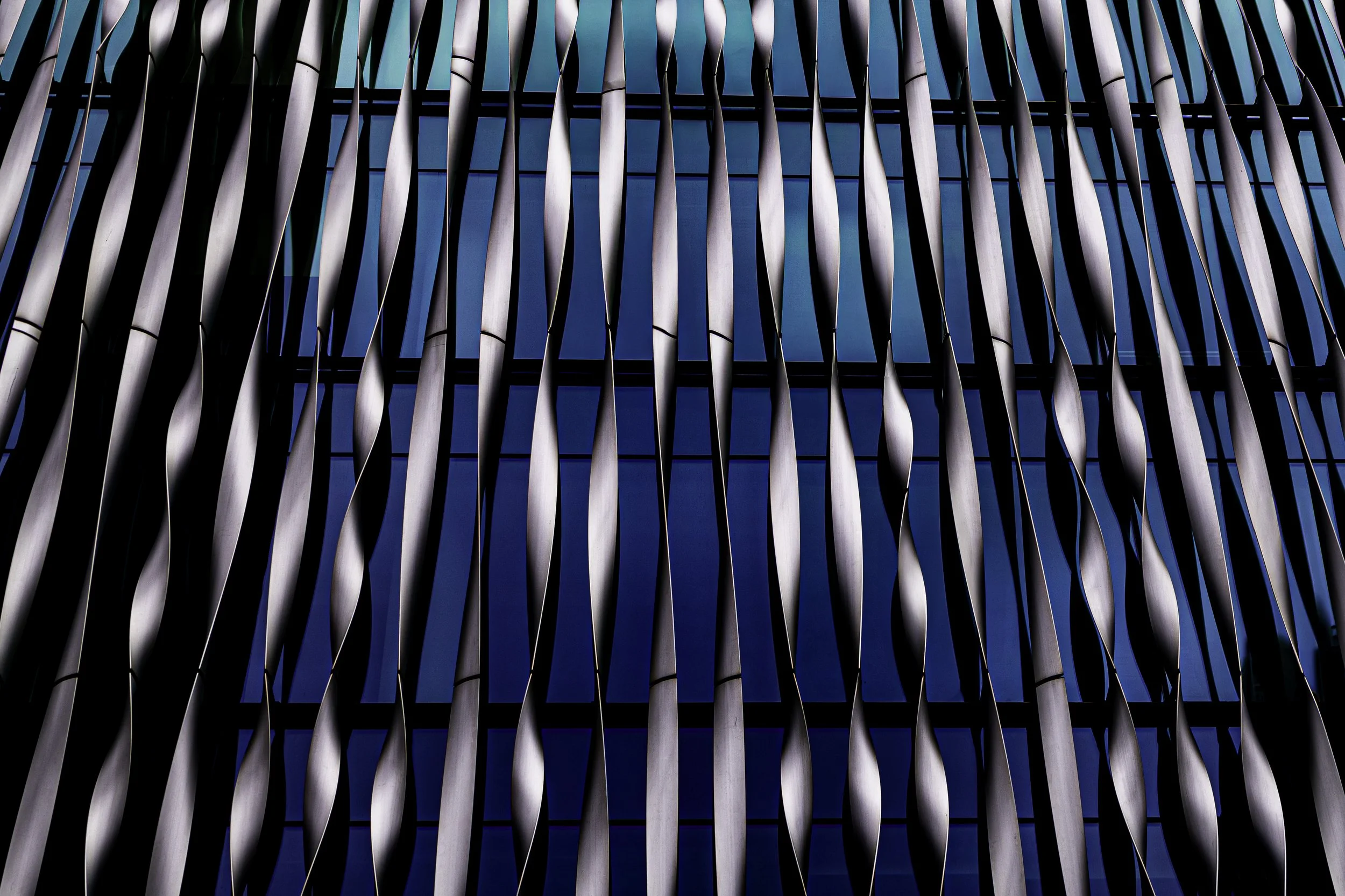 Close-up of a modern building's facade featuring vertical, wavy metal slats and glass windows.