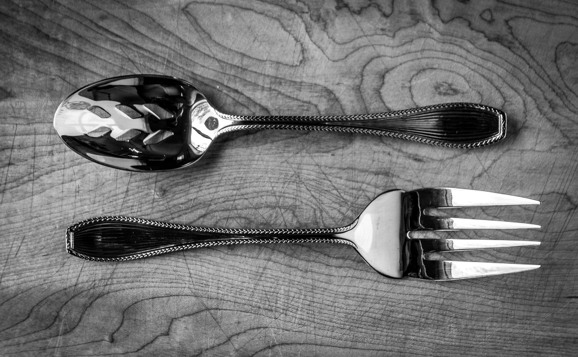 A polished silver fork and spoon with decorative handles placed parallel on a wooden surface.