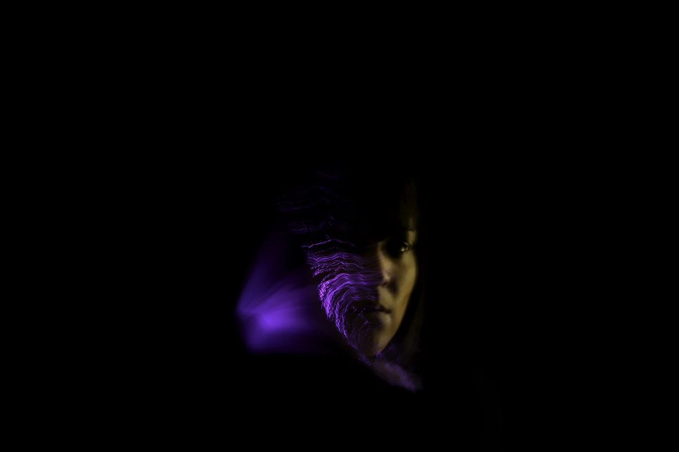 Partial portrait of a woman in darkness with purple and yellow light streaks across her face