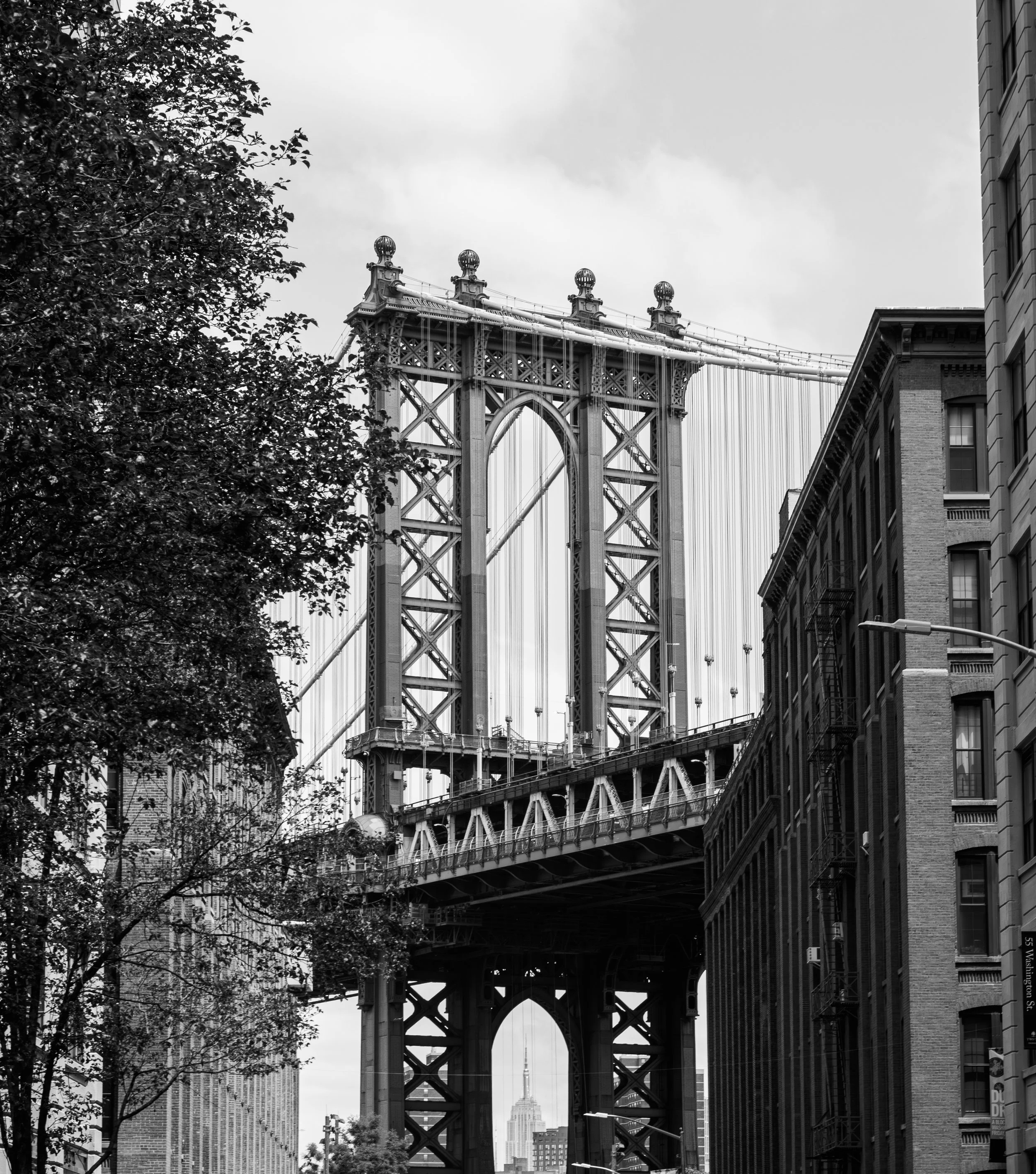 Black and white photo of the Manhattan Bridge in New York City with the Empire State Building visible in the background.