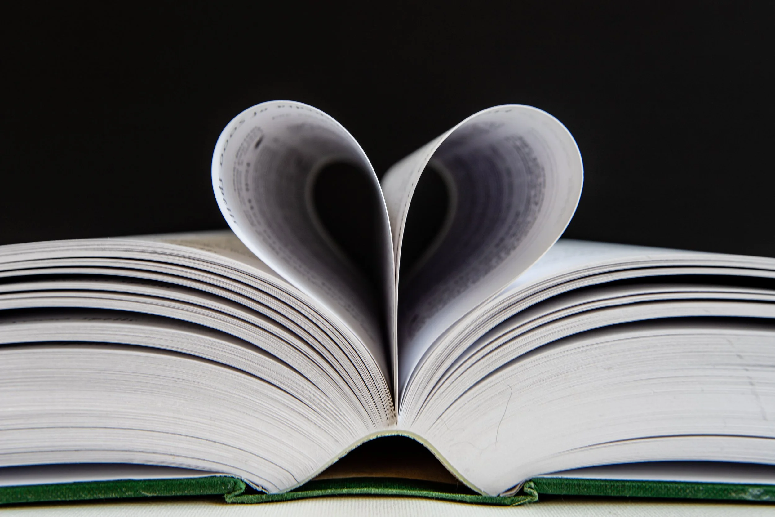 Open book with pages folded to create a heart shape against a black background.