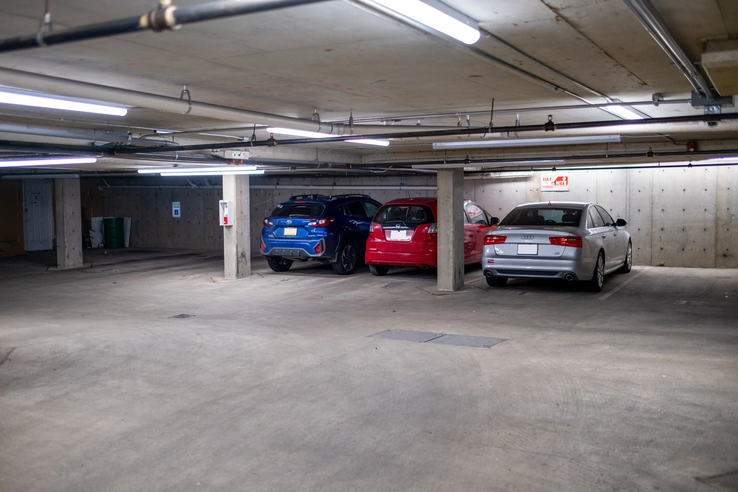 Underground parking garage with three parked cars and fluorescent ceiling lights.