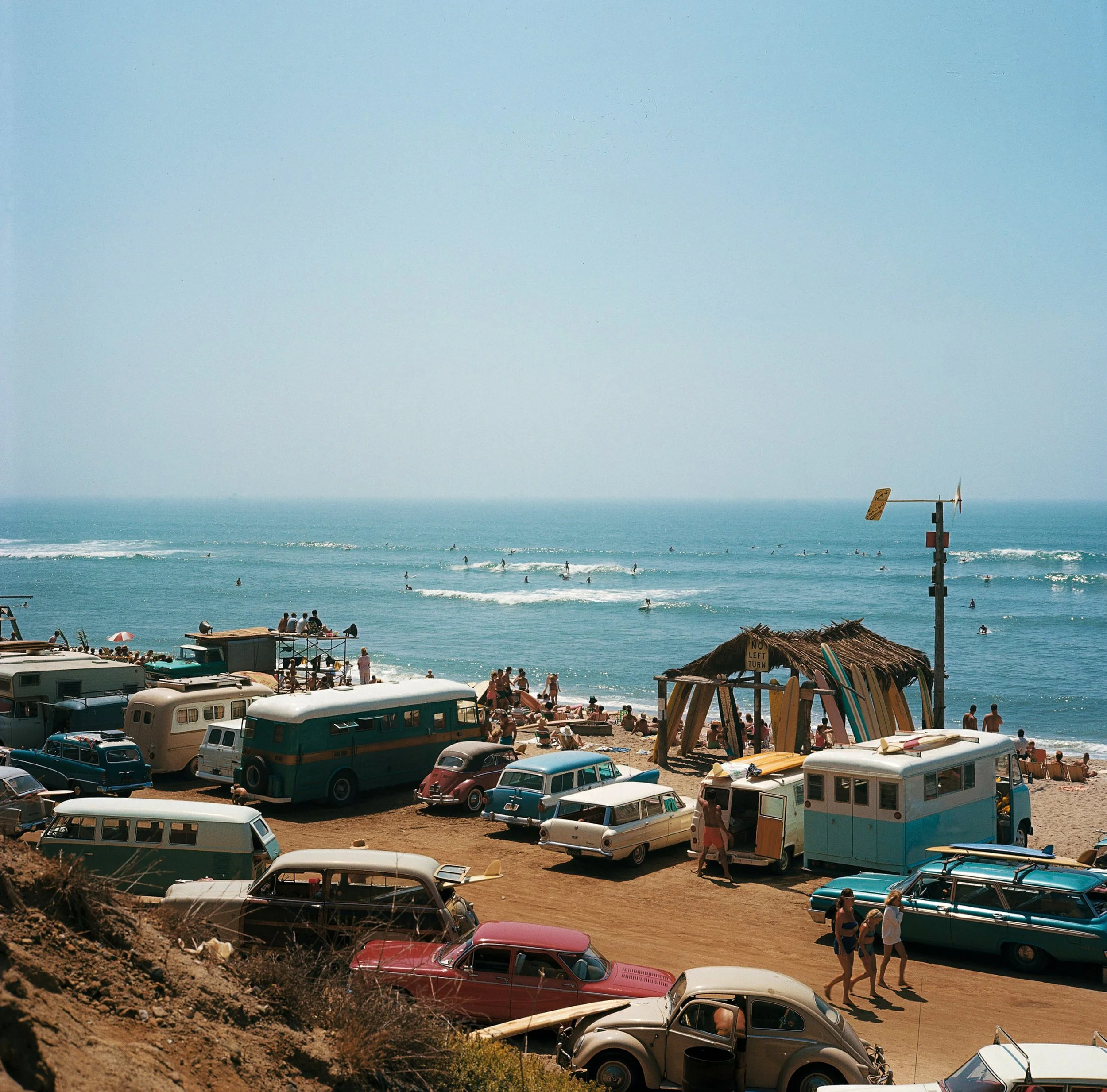 Beach scene with vintage cars parked on the sand, people relaxing, and surfers in the ocean.