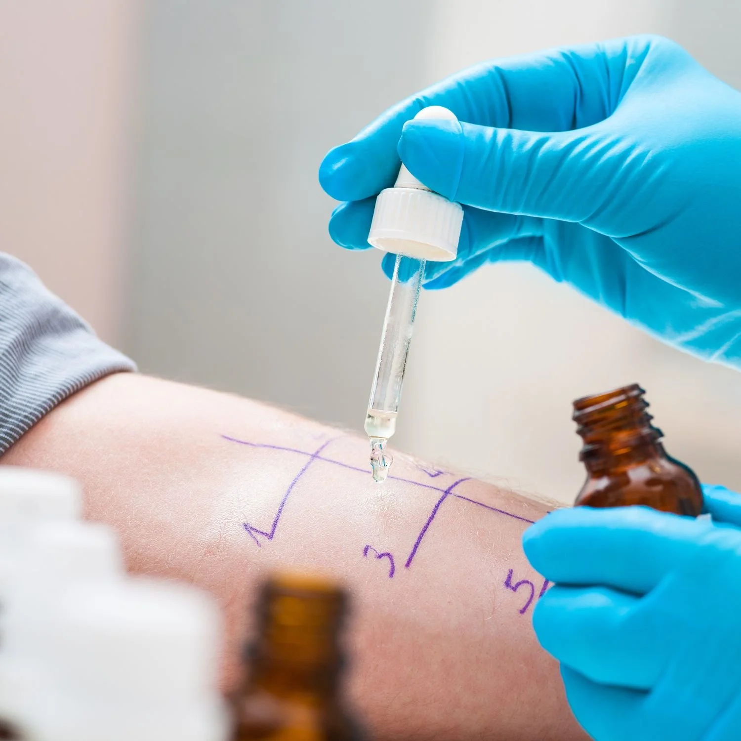 A medical professional wearing blue gloves is administering a vaccine or drawing blood from a patient's arm using a dropper and small glass vial.