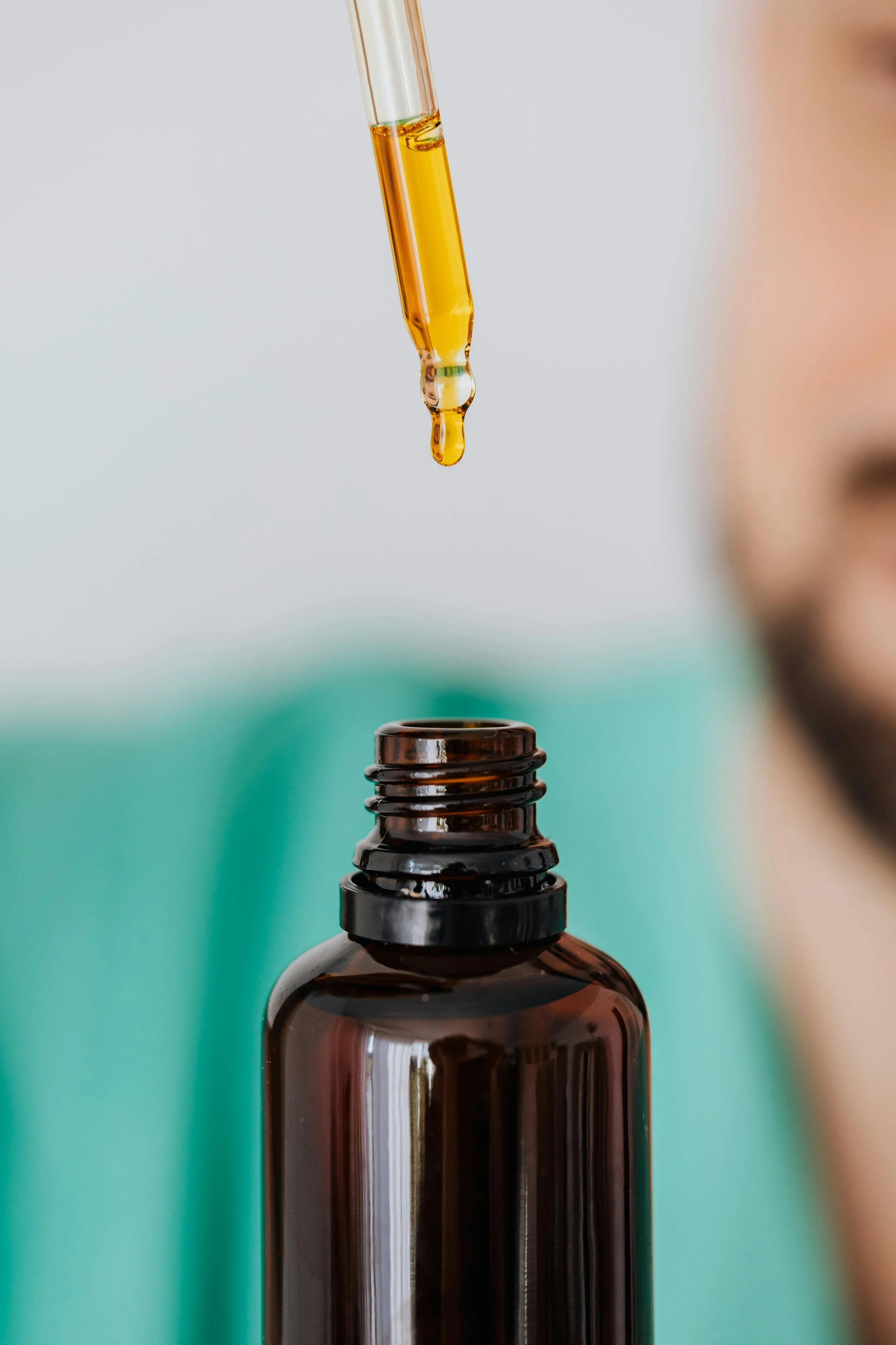 Close-up of a brown medicine bottle with a dropper releasing a droplet of yellow liquid into the bottle.