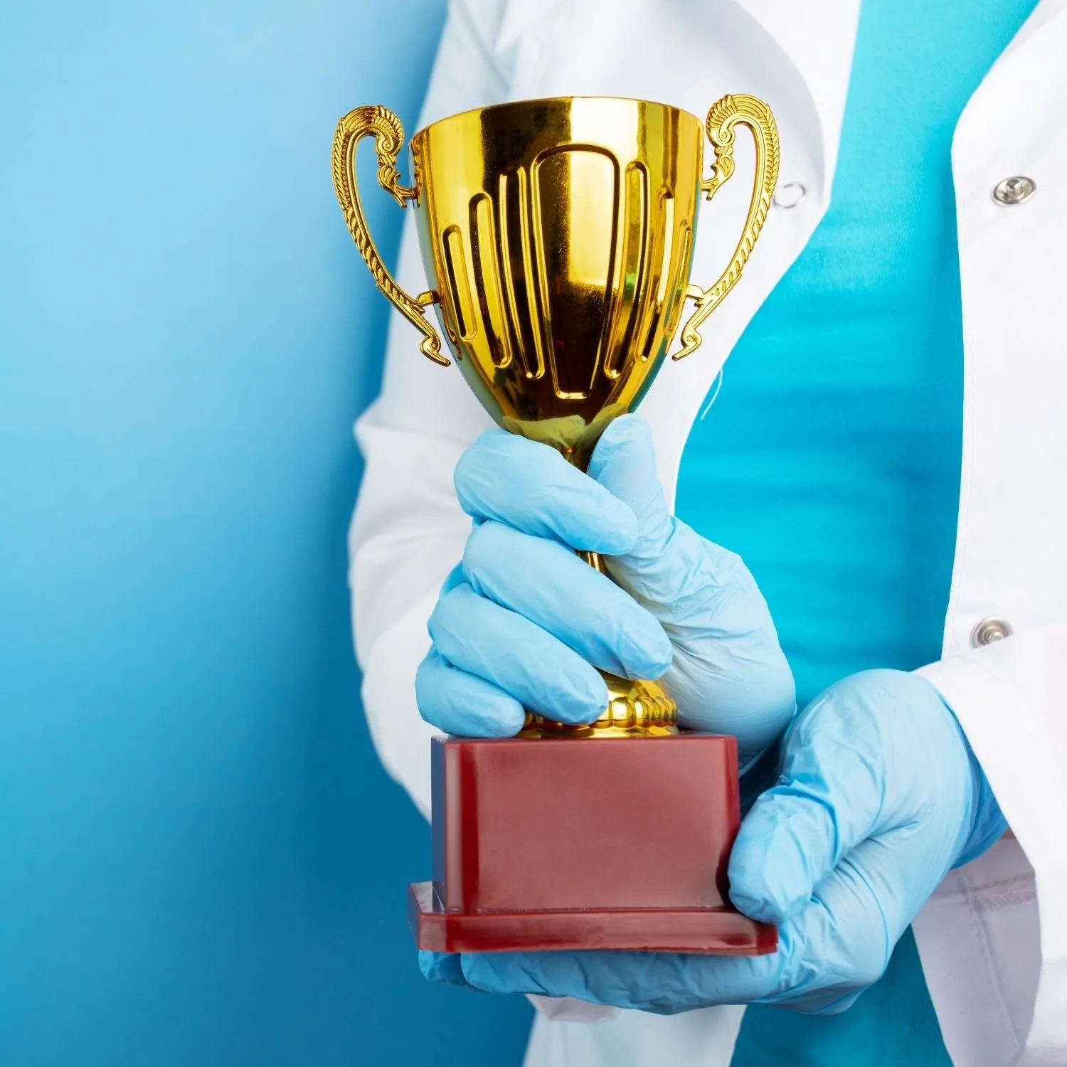 Person in medical scrubs and gloves holding a golden trophy.
