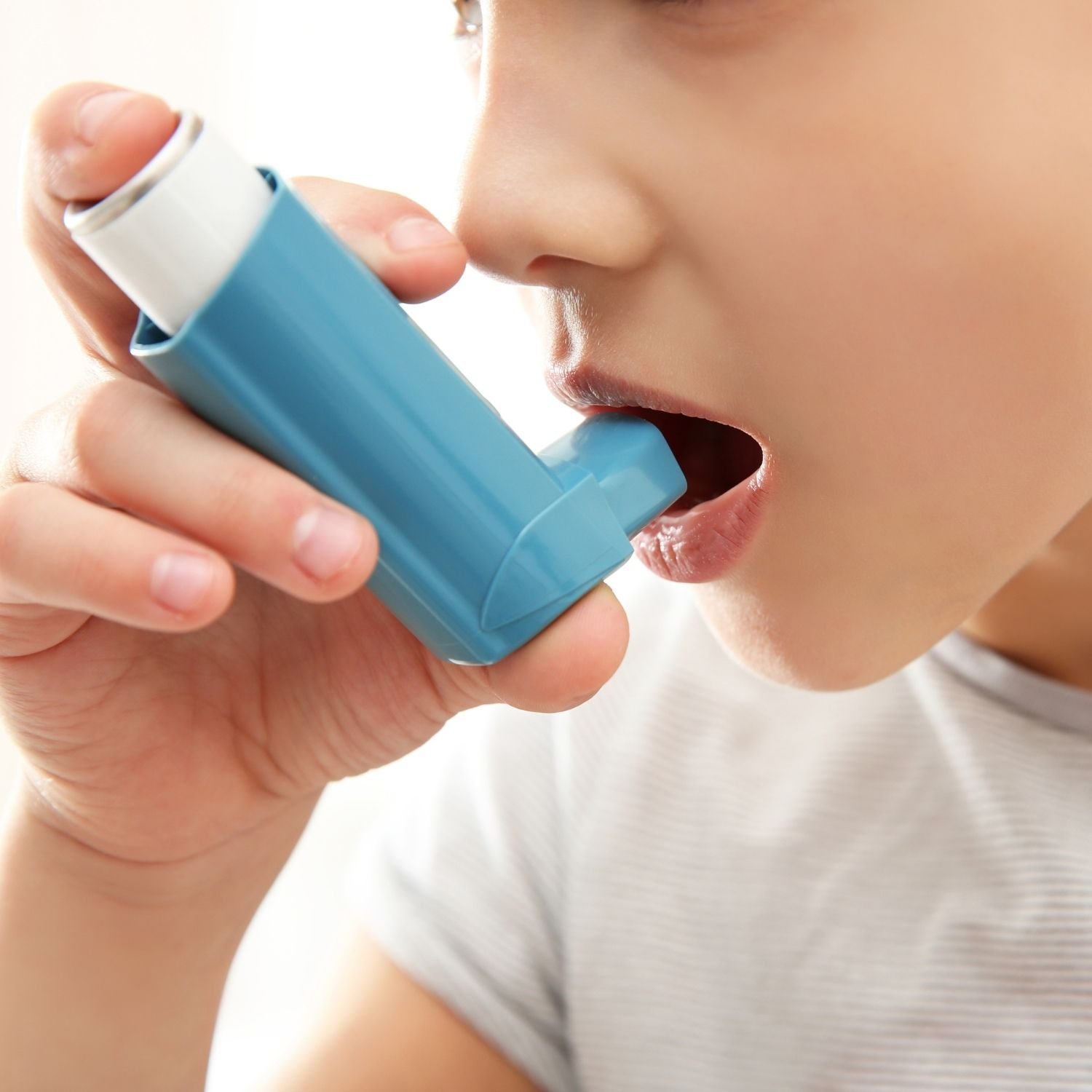 A child using a blue asthma inhaler, pressing it to inhale medication.