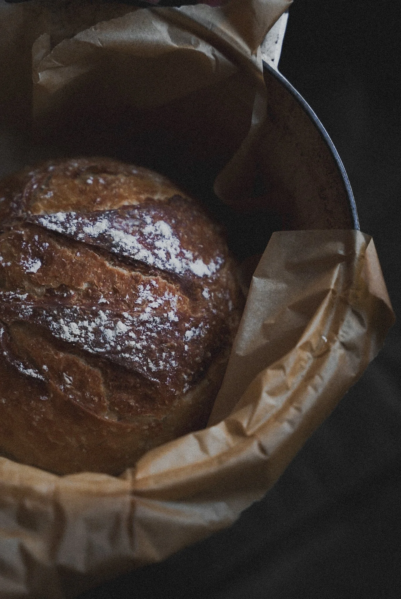A pastry with a golden brown crust dusted with powdered sugar, inside a paper bag in a metal container.