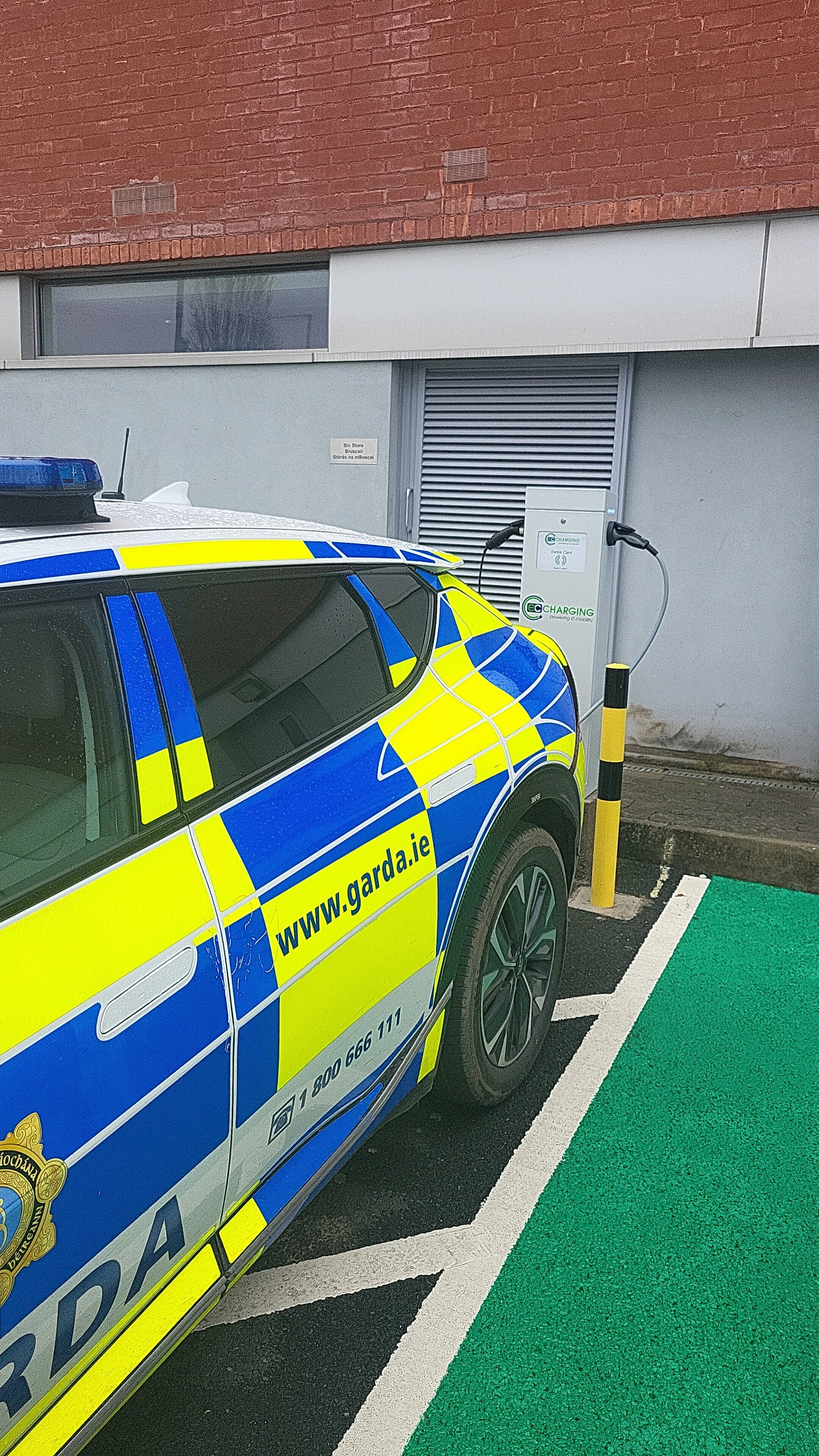Irish Garda police car parked at an electric vehicle charging station outside a building.
