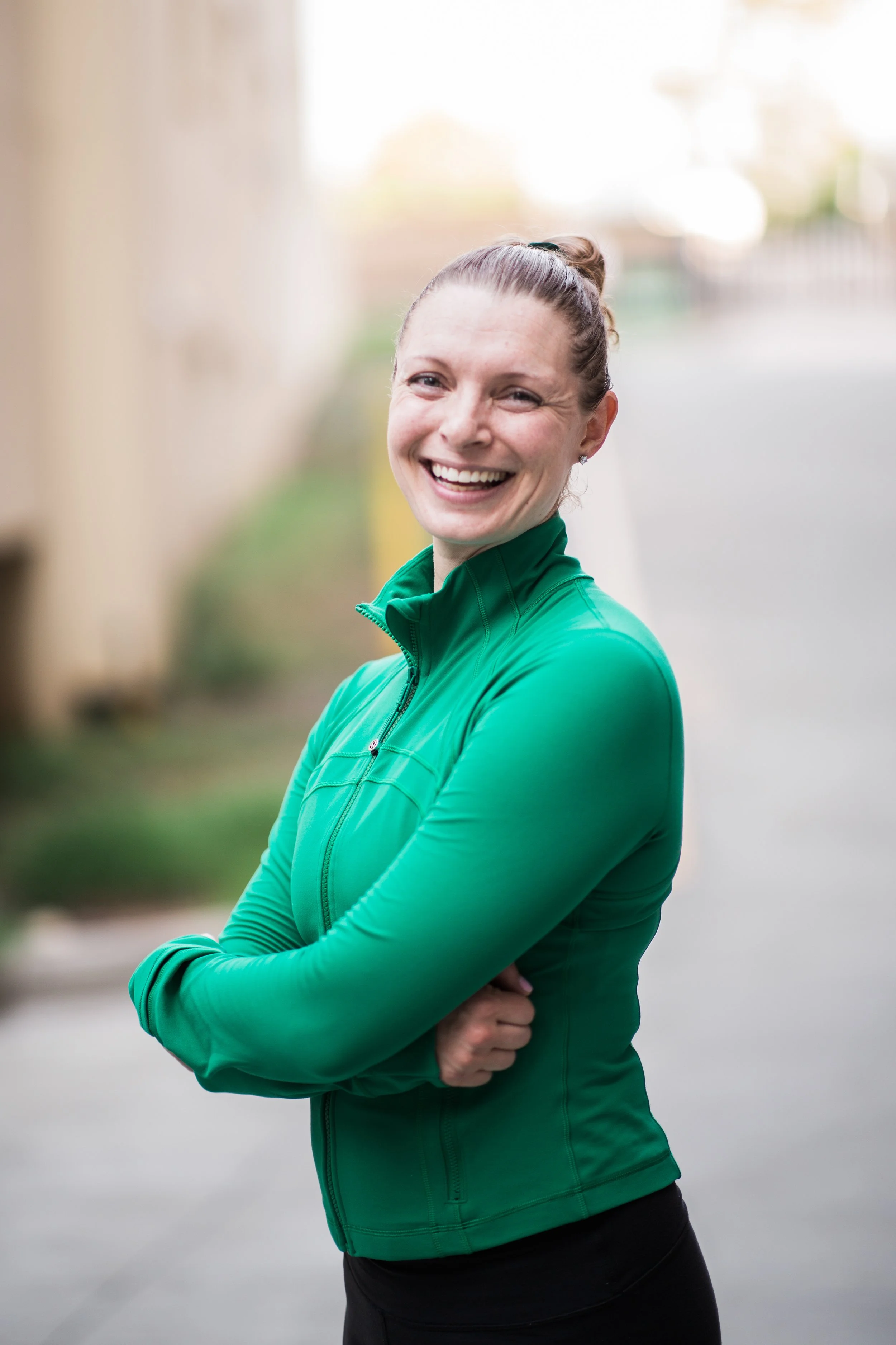 Smiling woman in green athletic jacket standing outdoors with arms crossed.