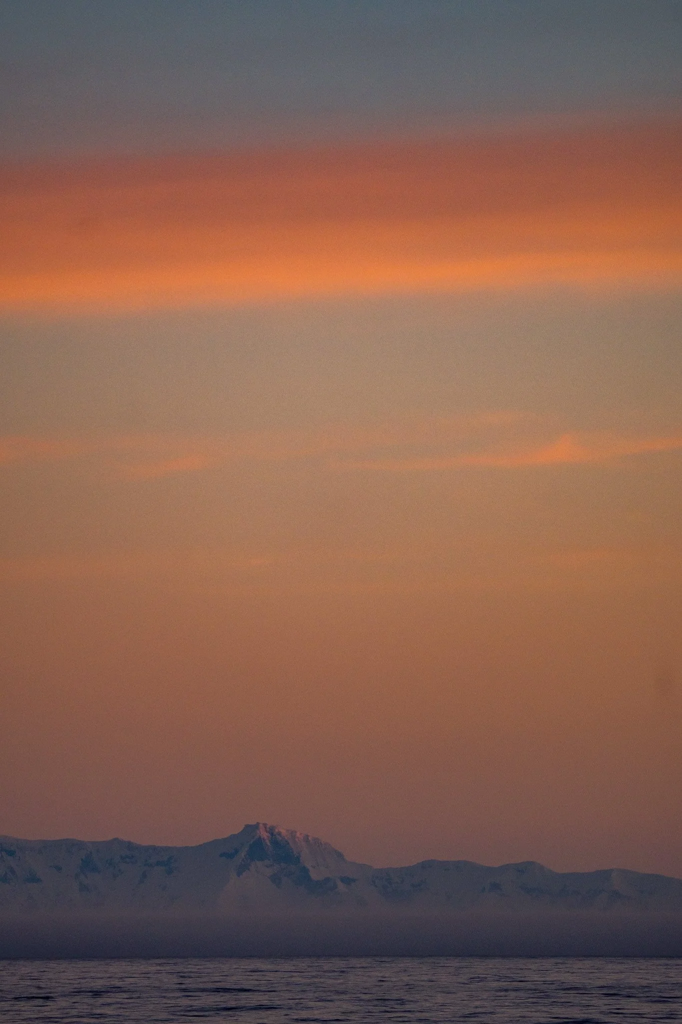 Sunset over snowy mountains and water with orange, pink, and purple sky.