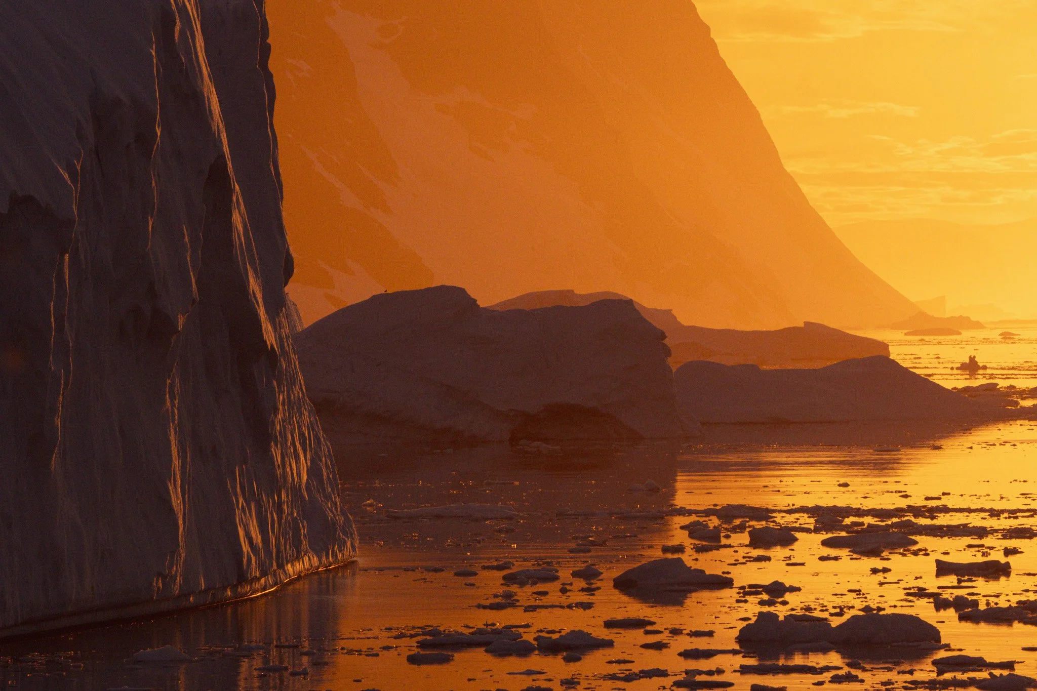 Sunset over icy waters with large icebergs and rocky cliffs in the foreground