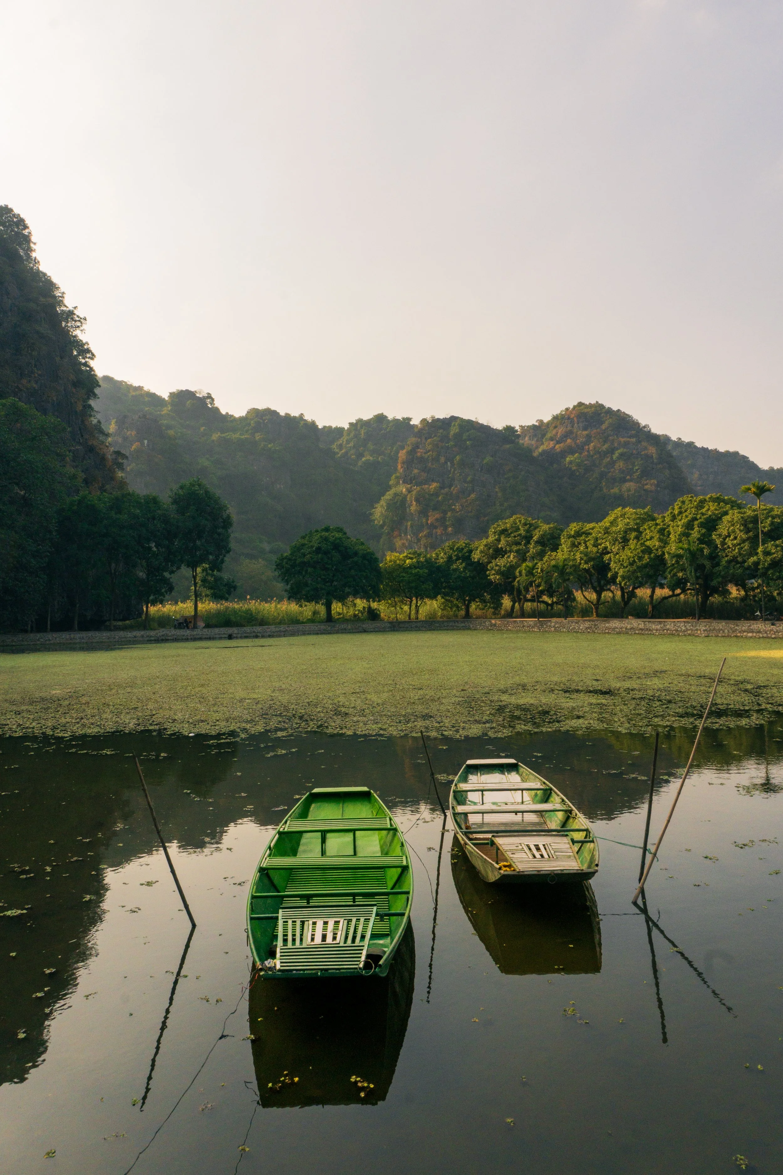 Two small boats floating on a calm lake surrounded by trees and hills.