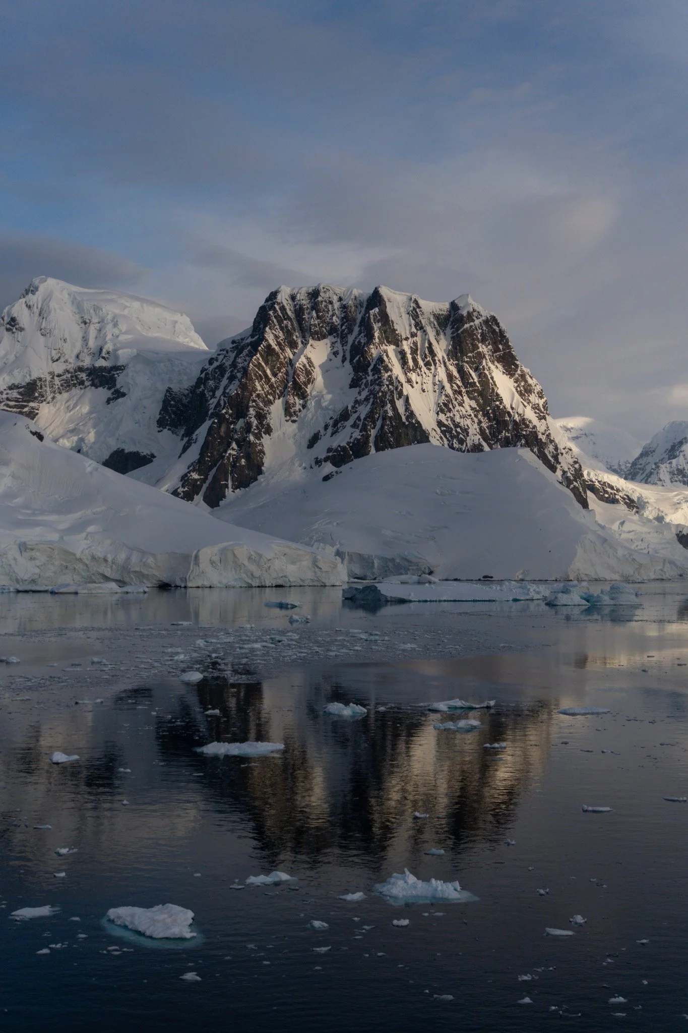 Snow-covered mountains reflecting on calm icy water with floating icebergs