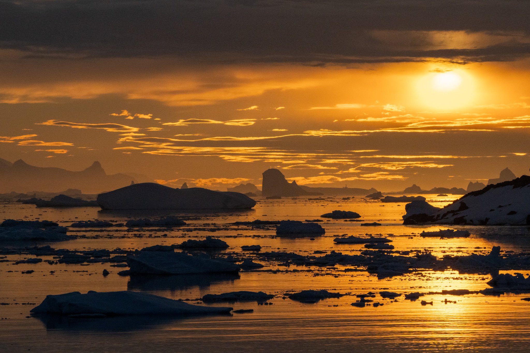 Sunset over icy water with floating icebergs and mountainous landscape in the distance