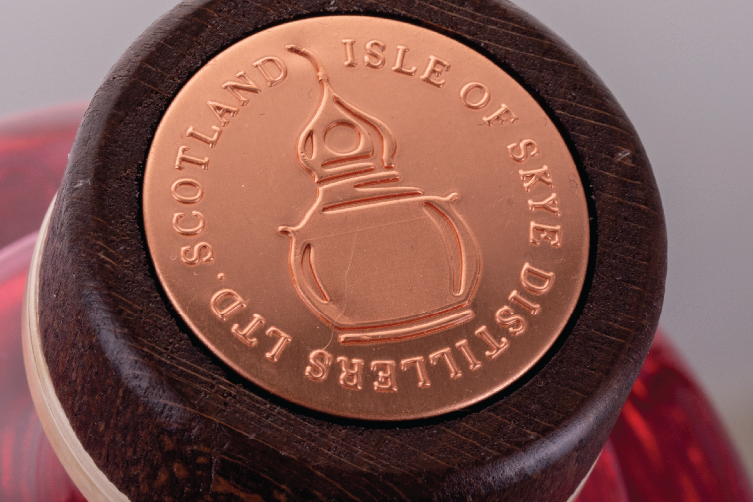 Close-up of a copper coin embedded in a dark wooden surface with the text 'LUXURY SKYE DISTILLERS, ISLE OF SKYE, SCOTLAND' and a line drawing of a distillation apparatus.