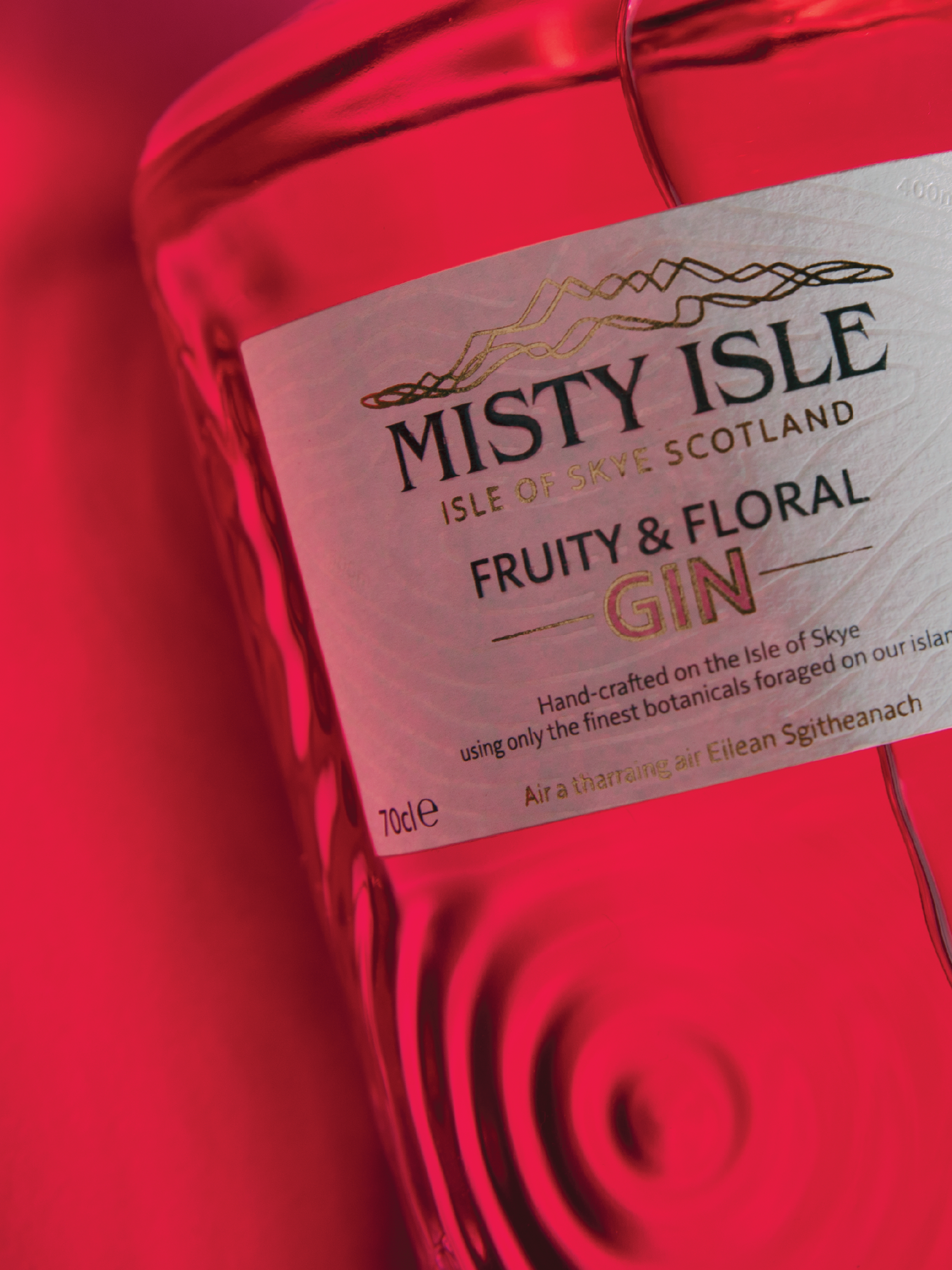 Close-up of a pink bottle of Misty Isle Fruity and Floral Gin on a pink background, showing the label with gold and black text.