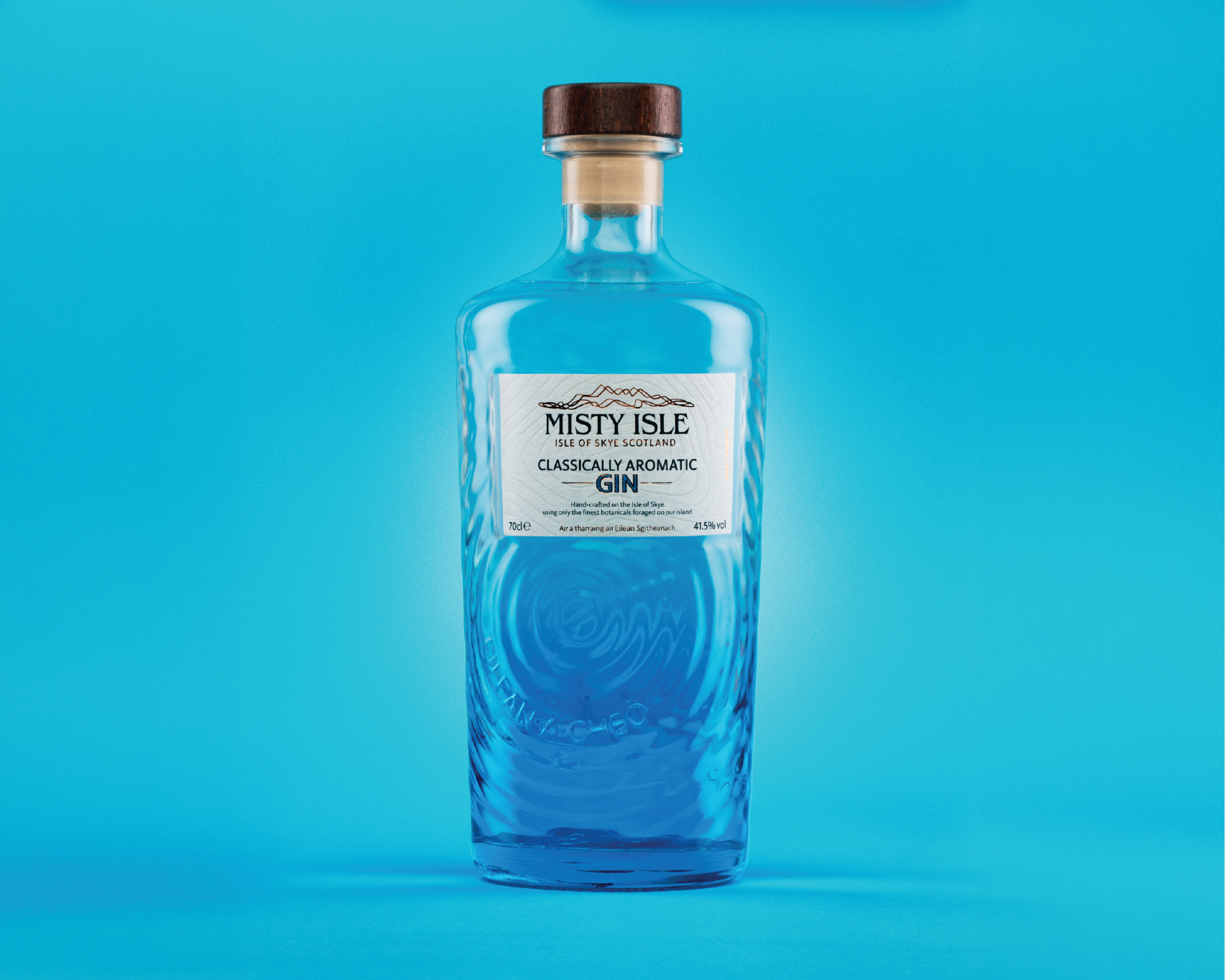 A clear glass bottle of Misty Isle classically aromatic gin with a wooden cap, standing against a blue background.