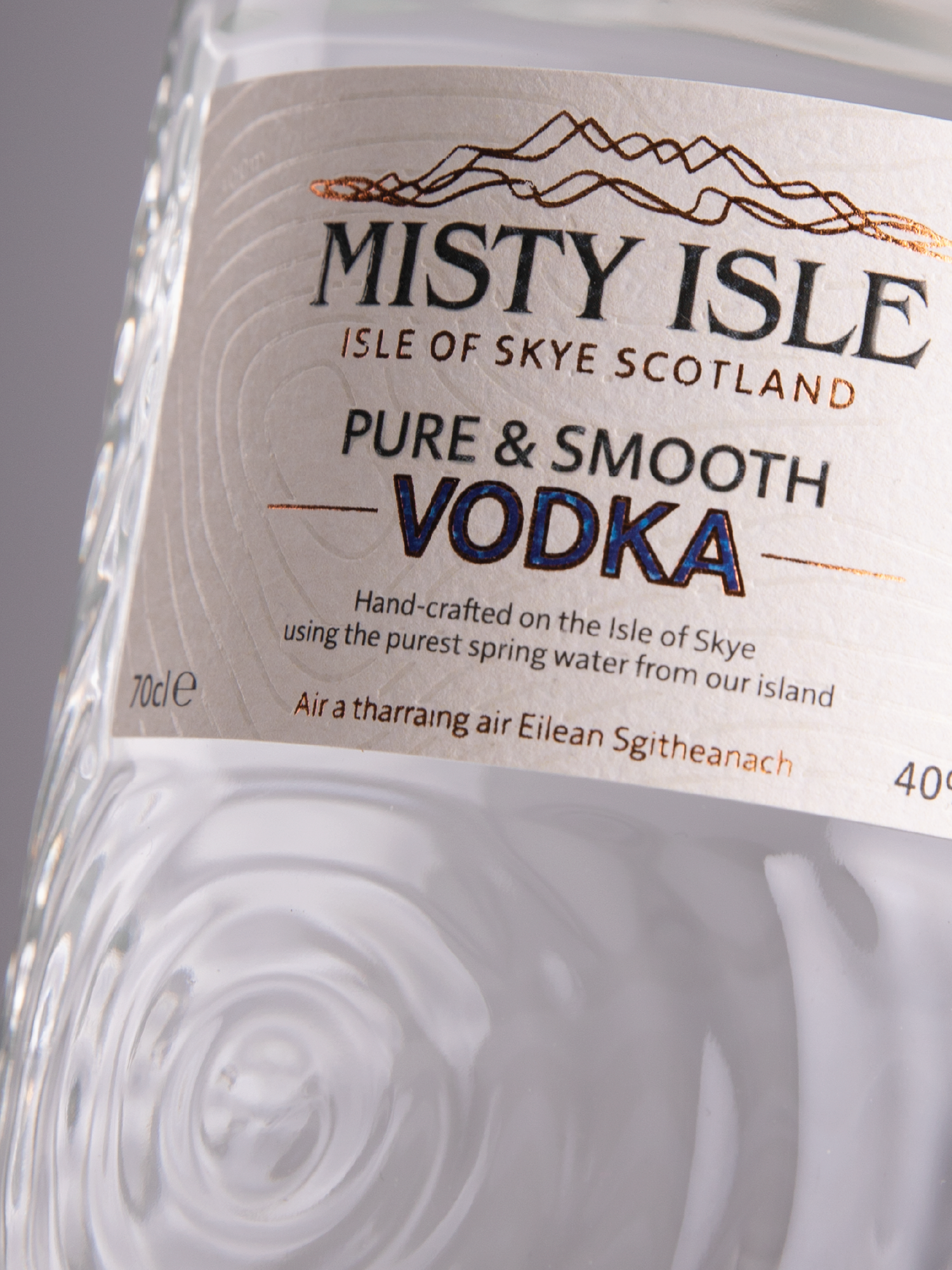 Close-up of a clear bottled vodka with a label that reads "Misty Isle Isle of Skye Scotland Pure & Smooth Vodka" in black and blue letters, featuring a mountainous illustration at the top.