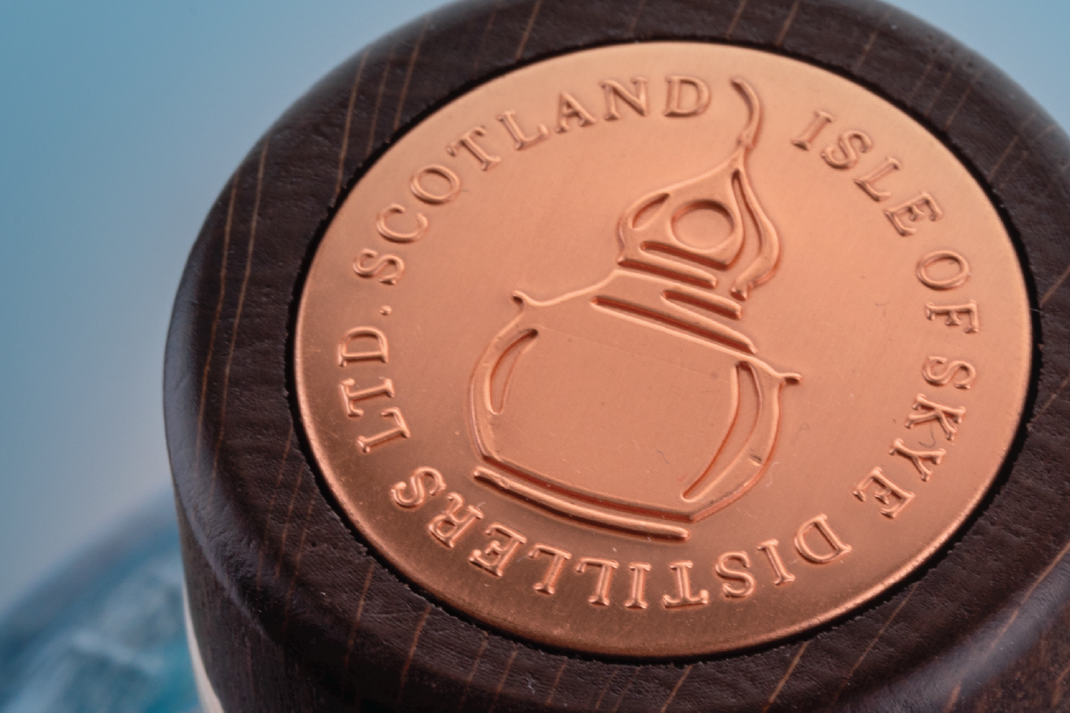 Close-up of a copper-colored medal or coin with a lighthouse and the words 'DISPLAYS, LTD. • COTLAND, ISLE OF SKYE, U.K.' engraved around the edge, mounted in a wooden holder.