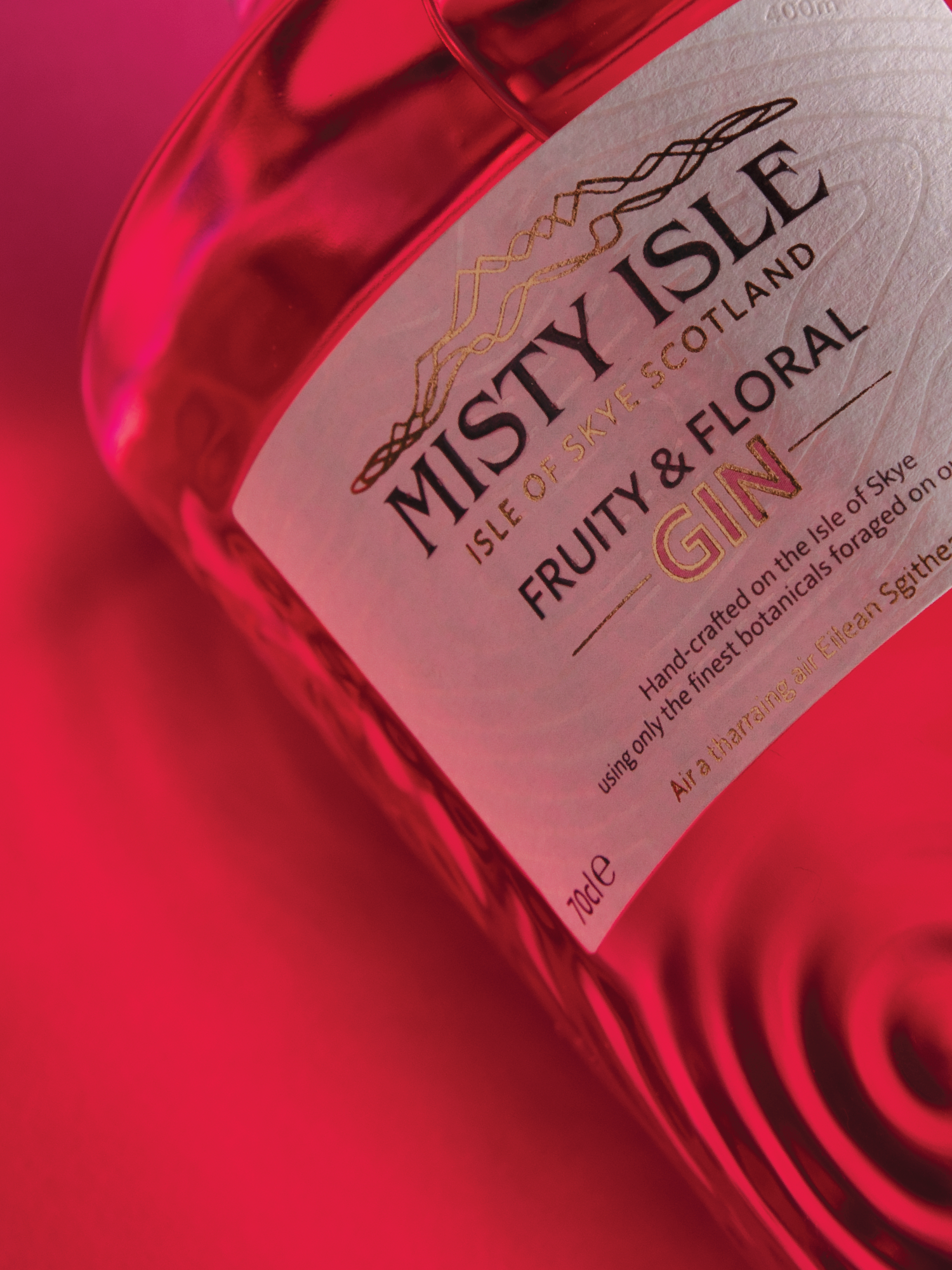 Close-up of a bottle of Misty Isle Fruity & Floral Gin, with pinkish-red background