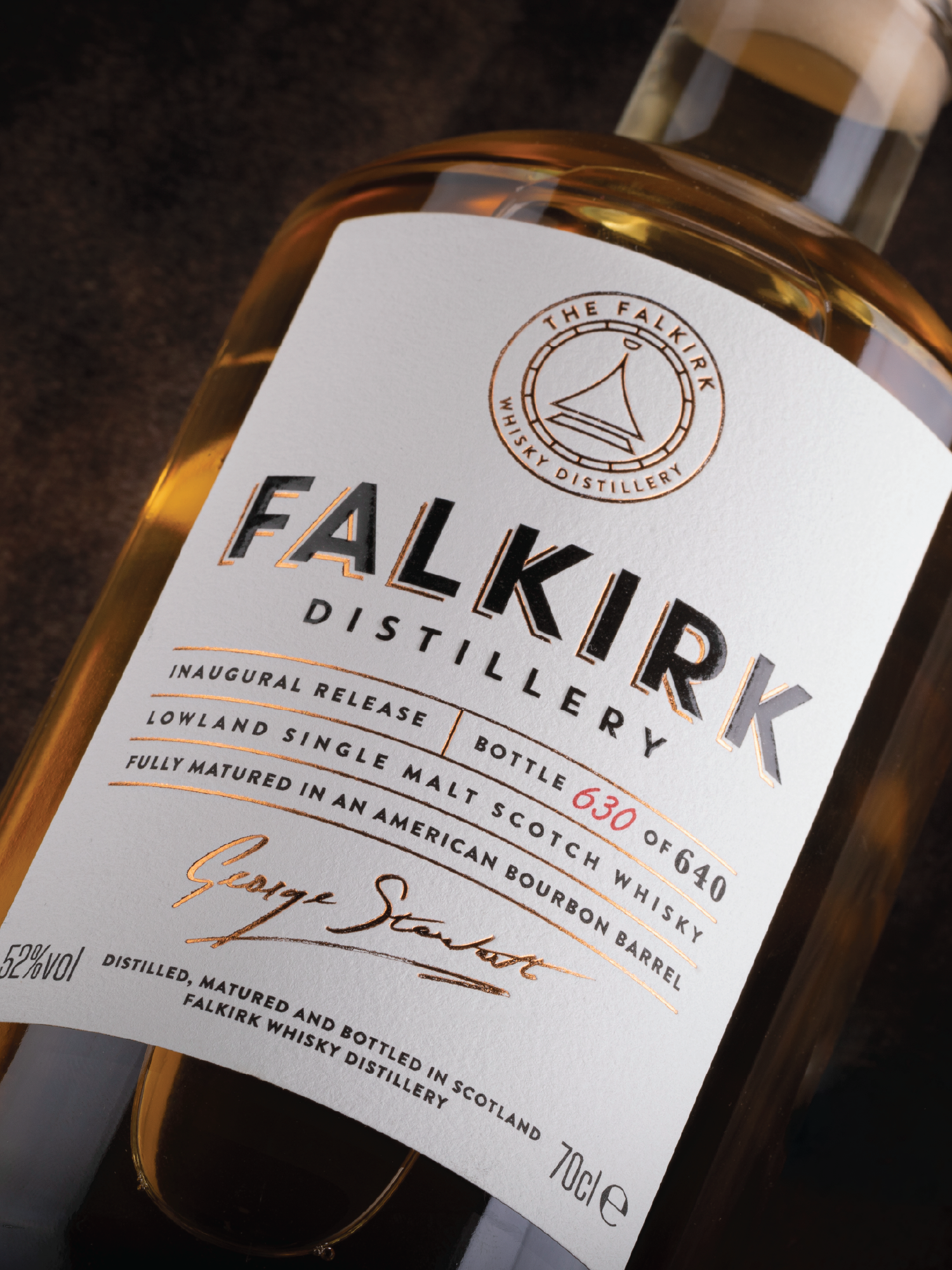A bottle of whisky from Falkirk Distillery with a white label, displaying the distillery's name, logo, and details about the whisky, including that it is a lowland single malt scotch whisky, fully matured in an American bourbon barrel, with 52% alcoh