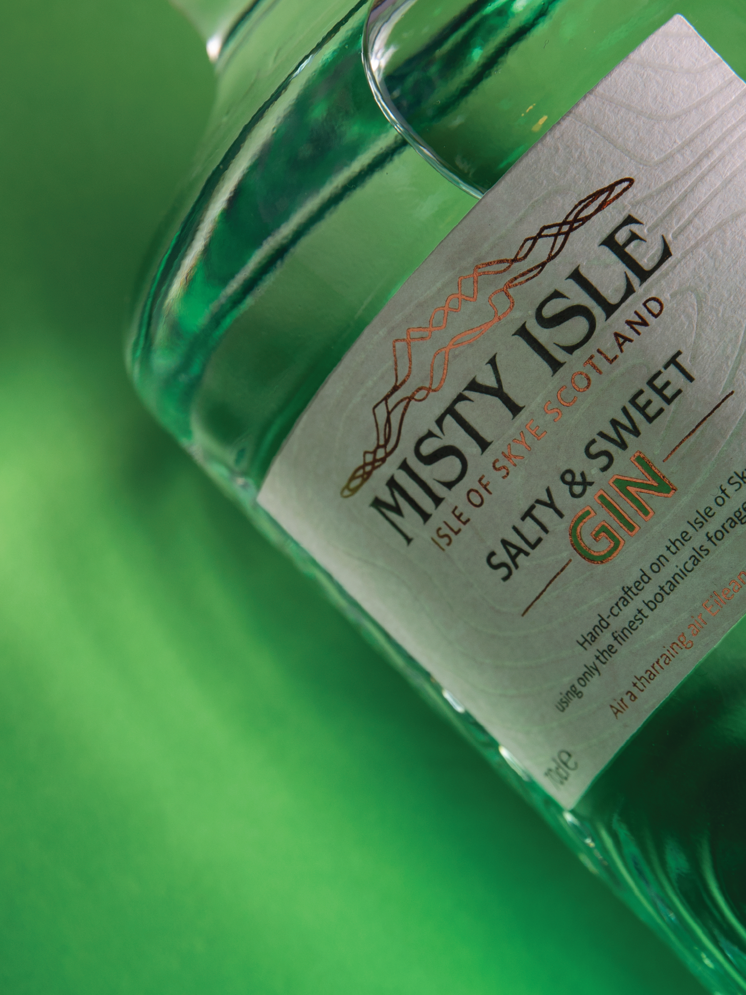 Close-up of a green glass bottle of Misety Isle Salty & Sweet GIN on a green surface.