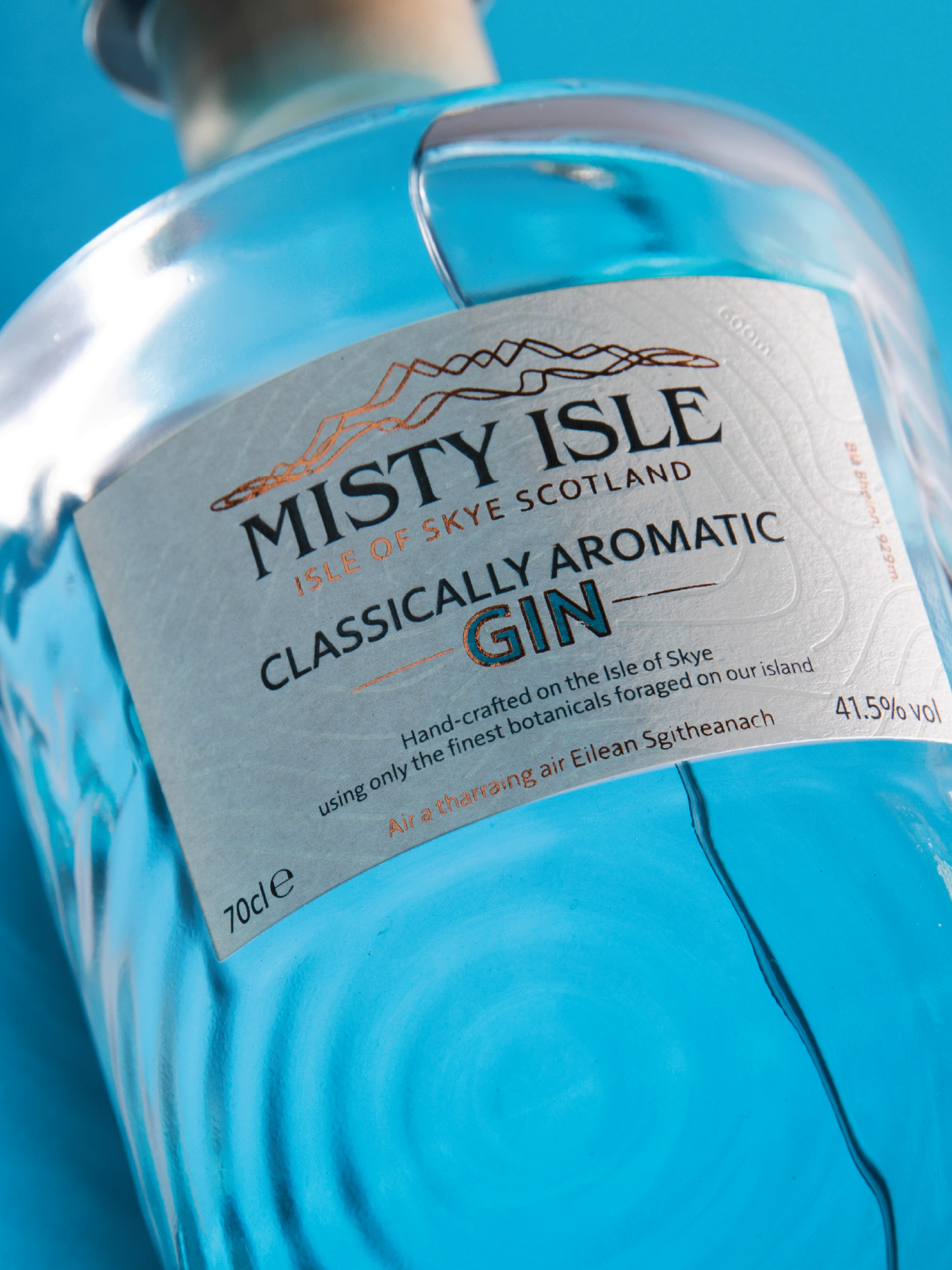 Close-up of a bottle of Misty Isle classic aromatic gin with blue liquid inside, set against a blue background.