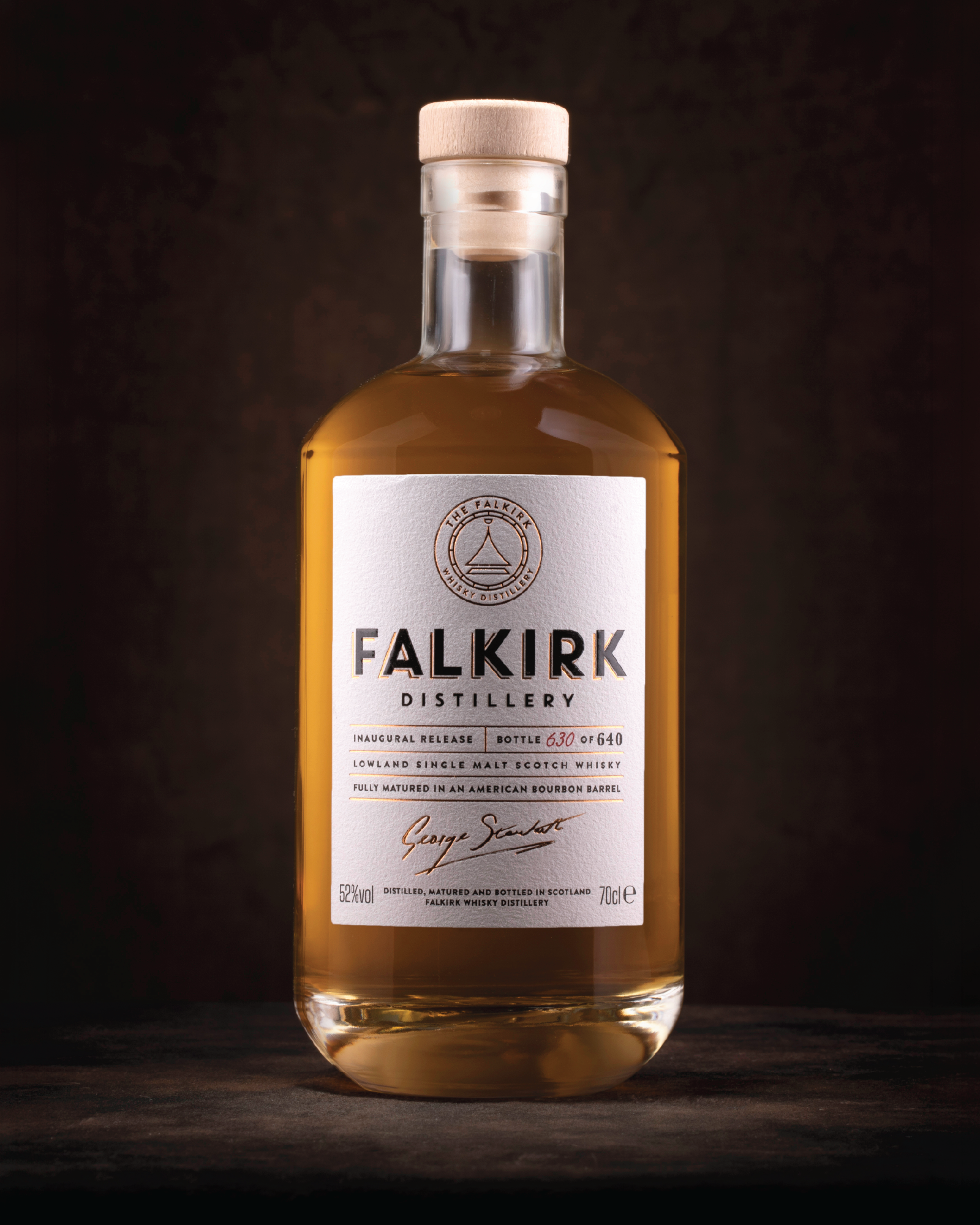 A bottle of Falkirk Distillery whisky with a white label, wooden cap, and amber liquid inside, set against a dark background.