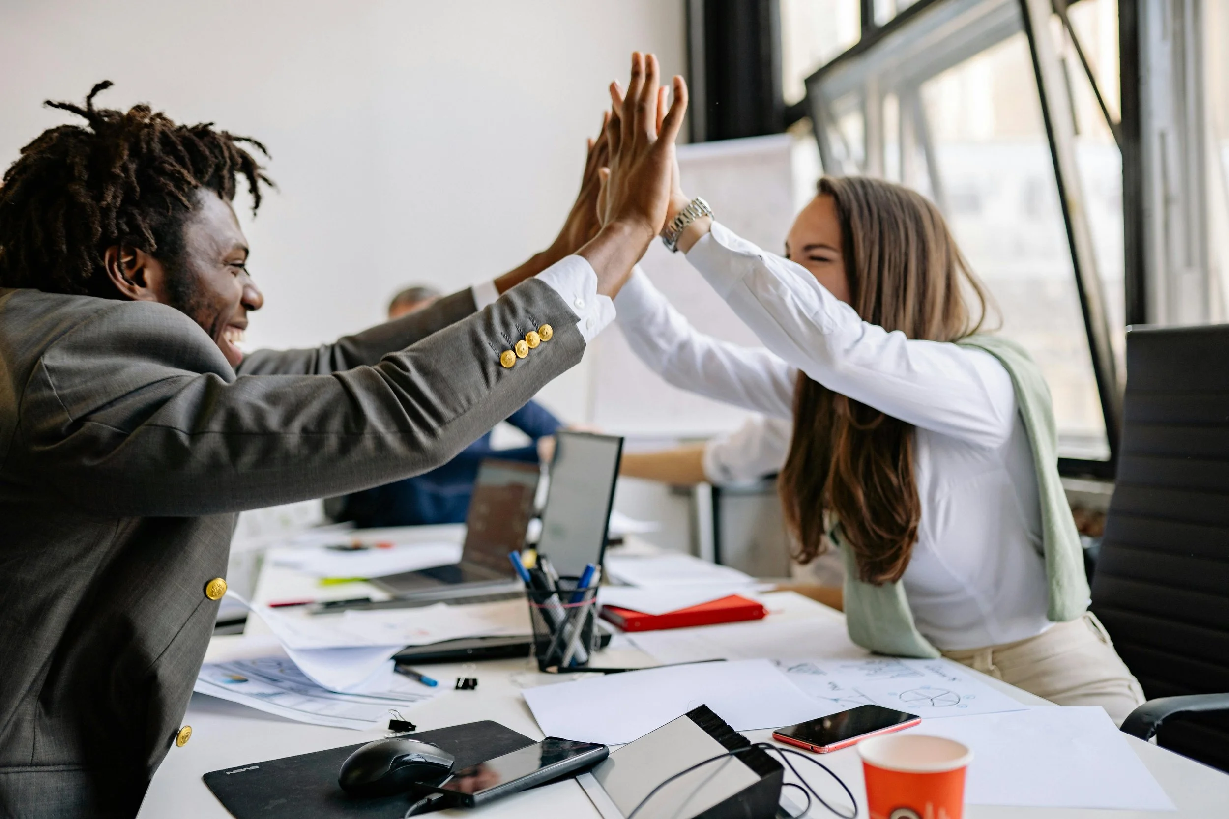 Two colleagues celebrating a successful compliance milestone with a high five in a professional office setting