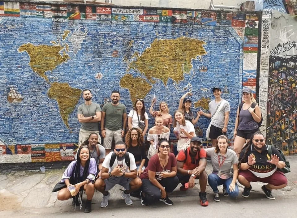 Travelers posing together in front of a tiled map mural.