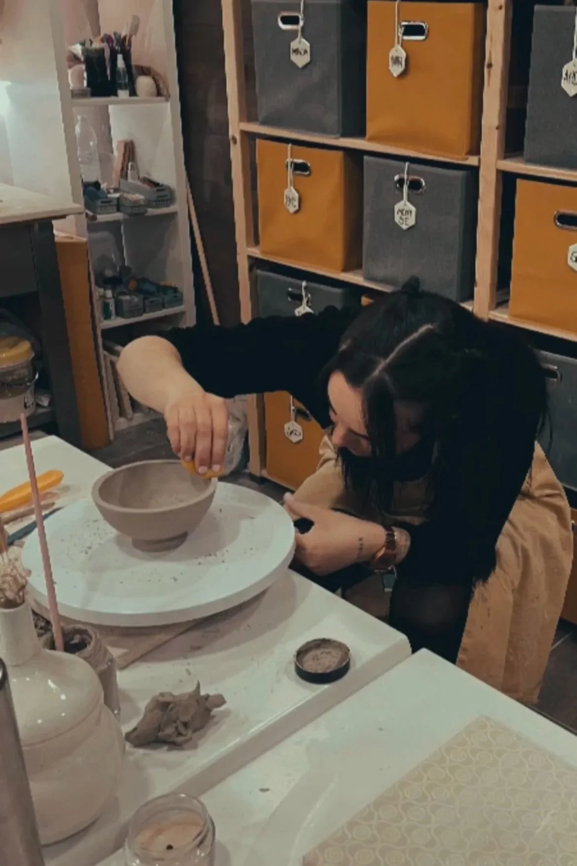 Una mujer decorando una cerámica en un taller de arte, rodeada de utensilios y materiales de pintura y escultura.