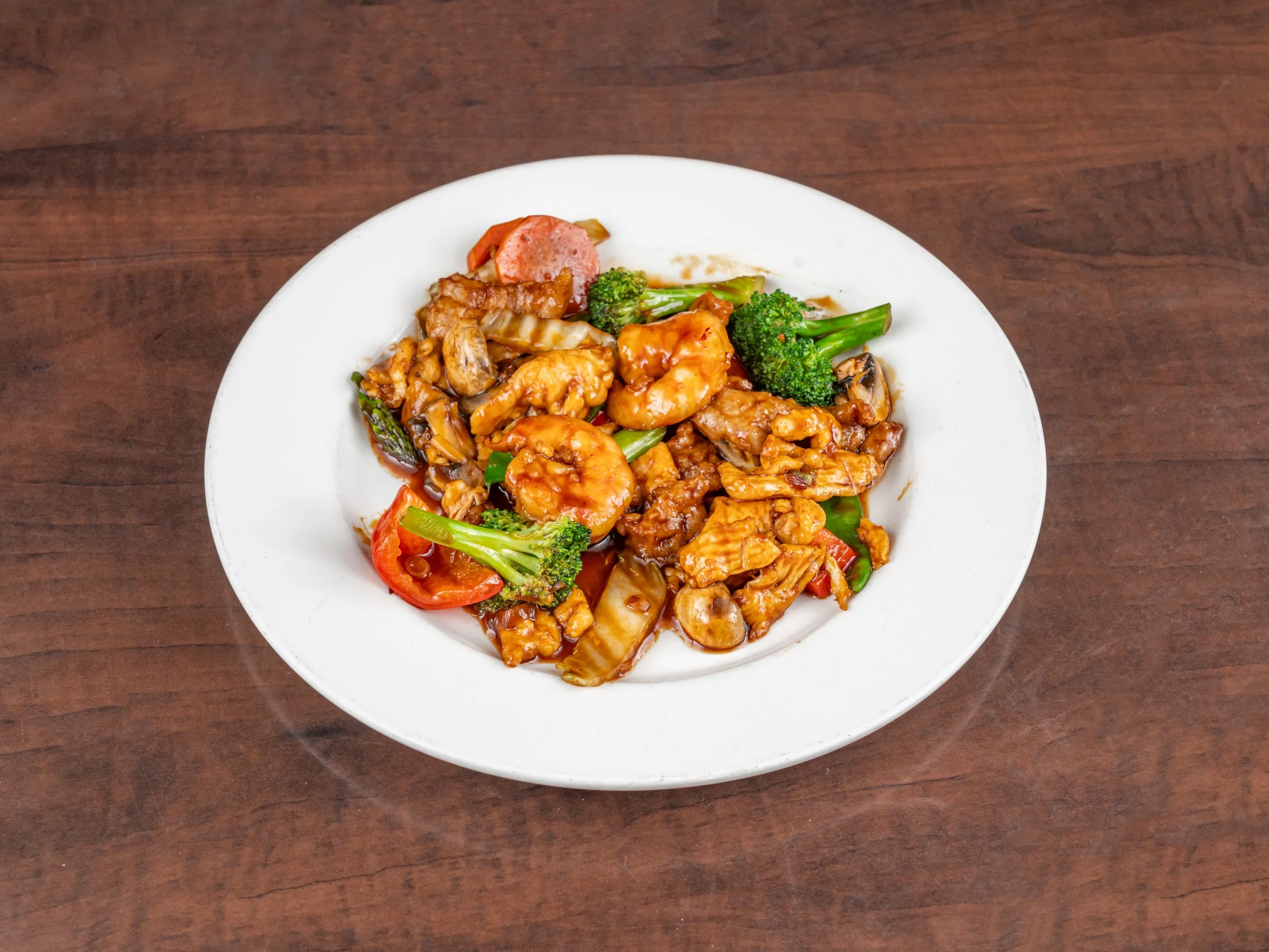 A white plate with stir-fried vegetables and shrimp on a wooden surface.