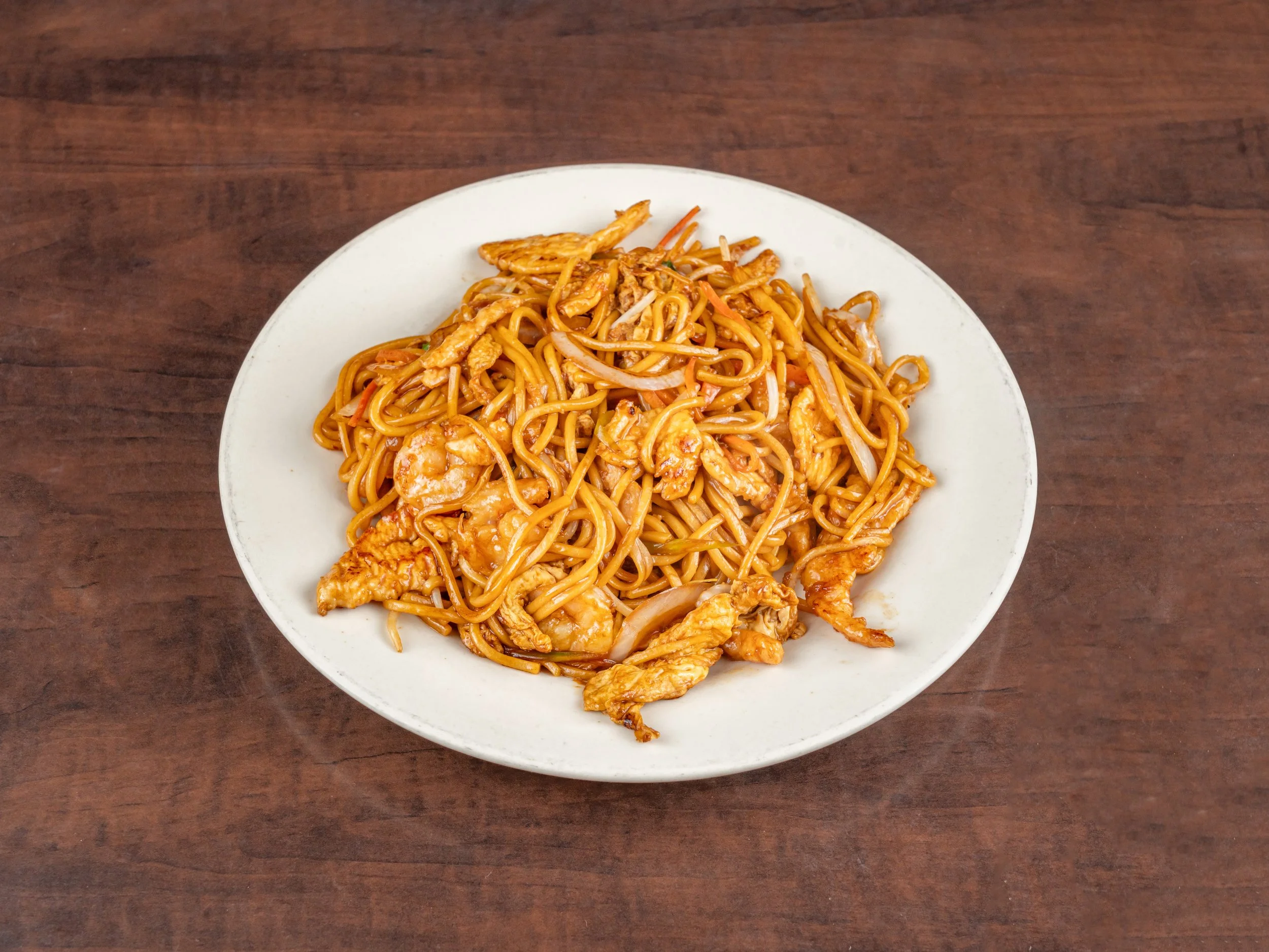 Plate of stir-fried noodles with chicken and vegetables on a wooden table.