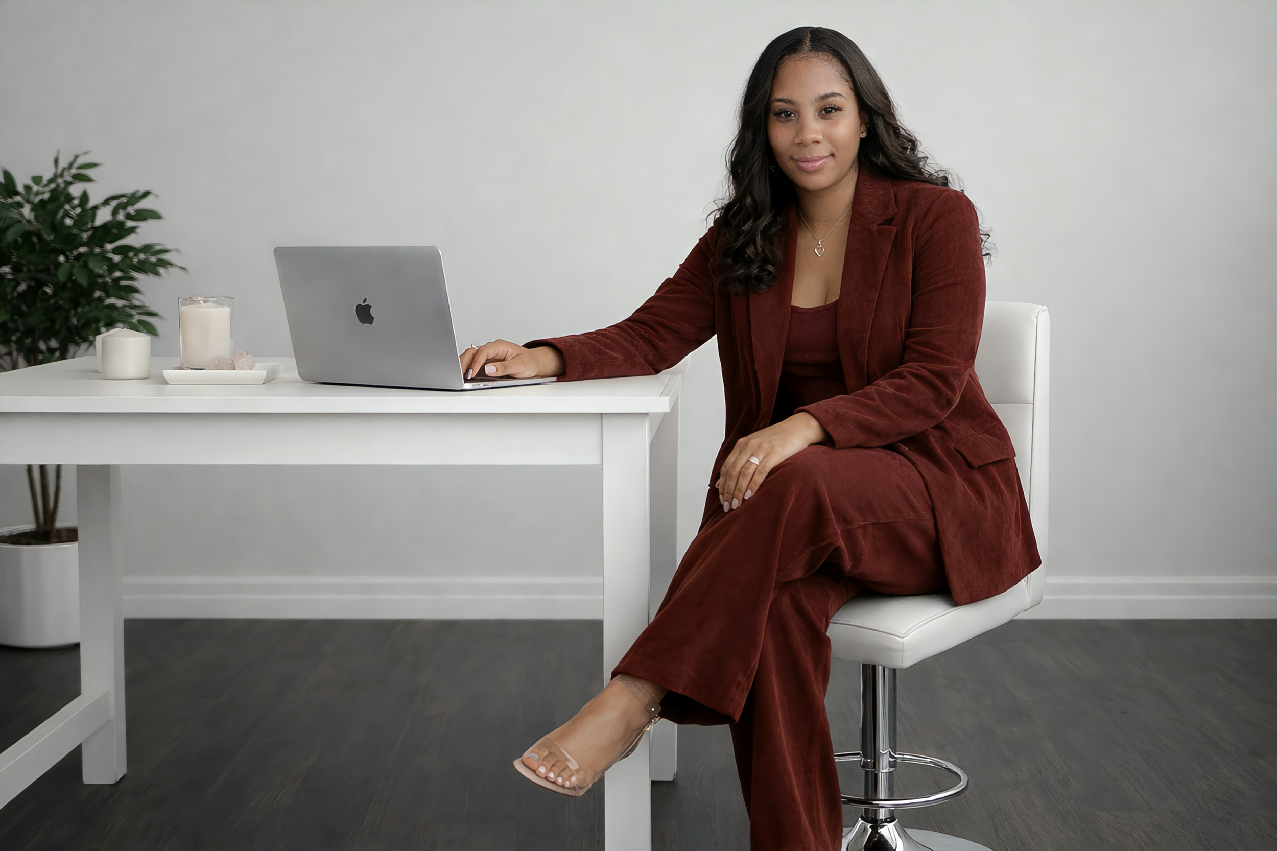 Anissia in a maroon suit seated at a modern desk, representing empowerment, confidence, and aligned leadership in transformational coaching.