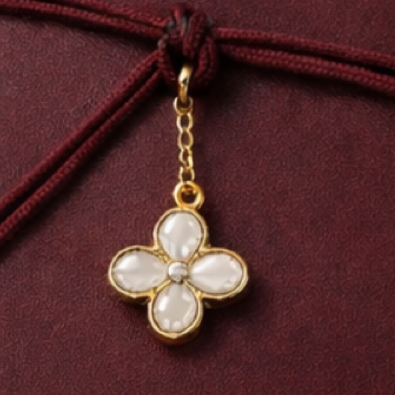 Gold necklace with a flower-shaped pendant featuring white petals, hanging against a maroon fabric background.