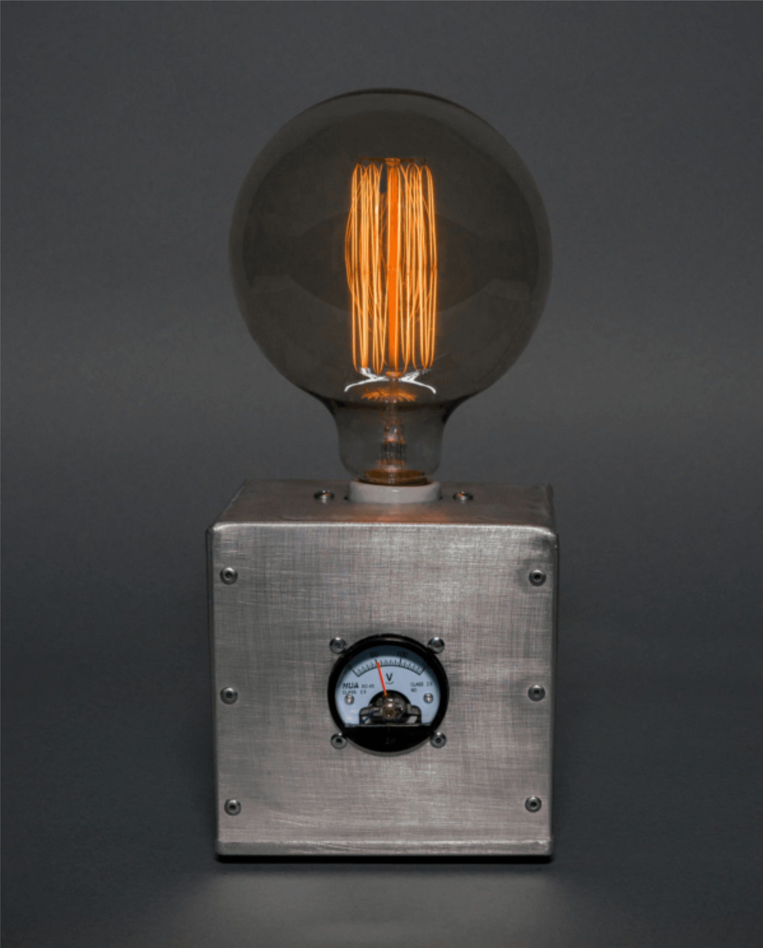An Edison-style filament light bulb mounted on a metallic panel with a voltmeter below it, against a dark background.