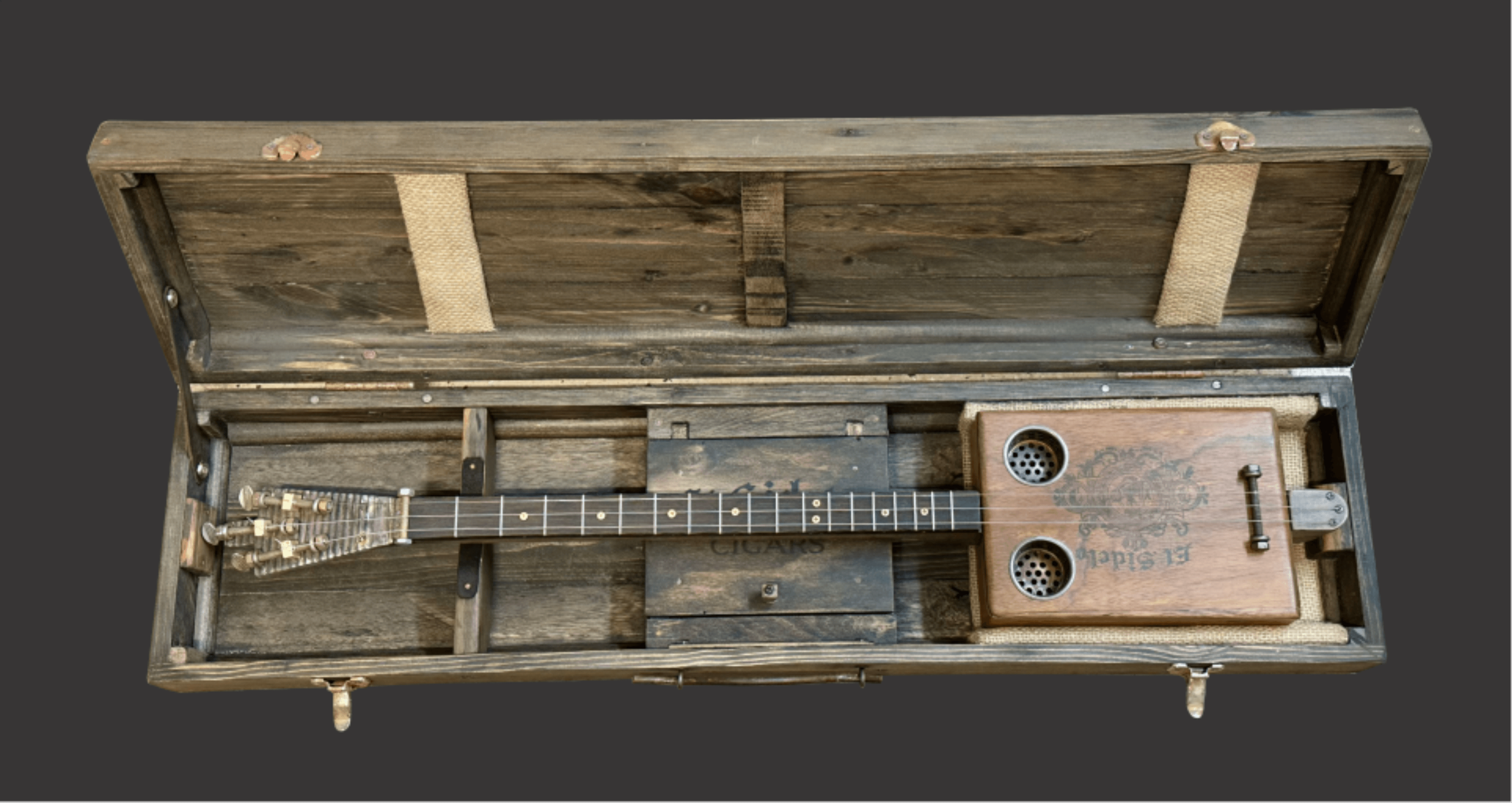 An open wooden cigar box converted into a miniature guitar with visible strings and tuning pegs.