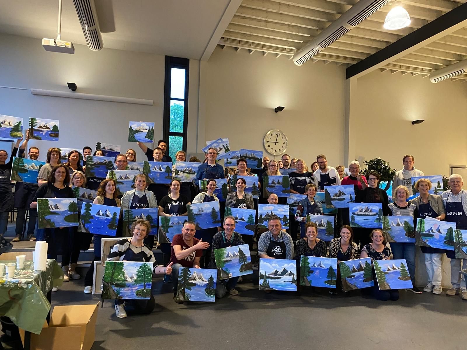 Groep mensen met kunstwerken van een landschap met water, bergen en bomen in een indoor locatie.