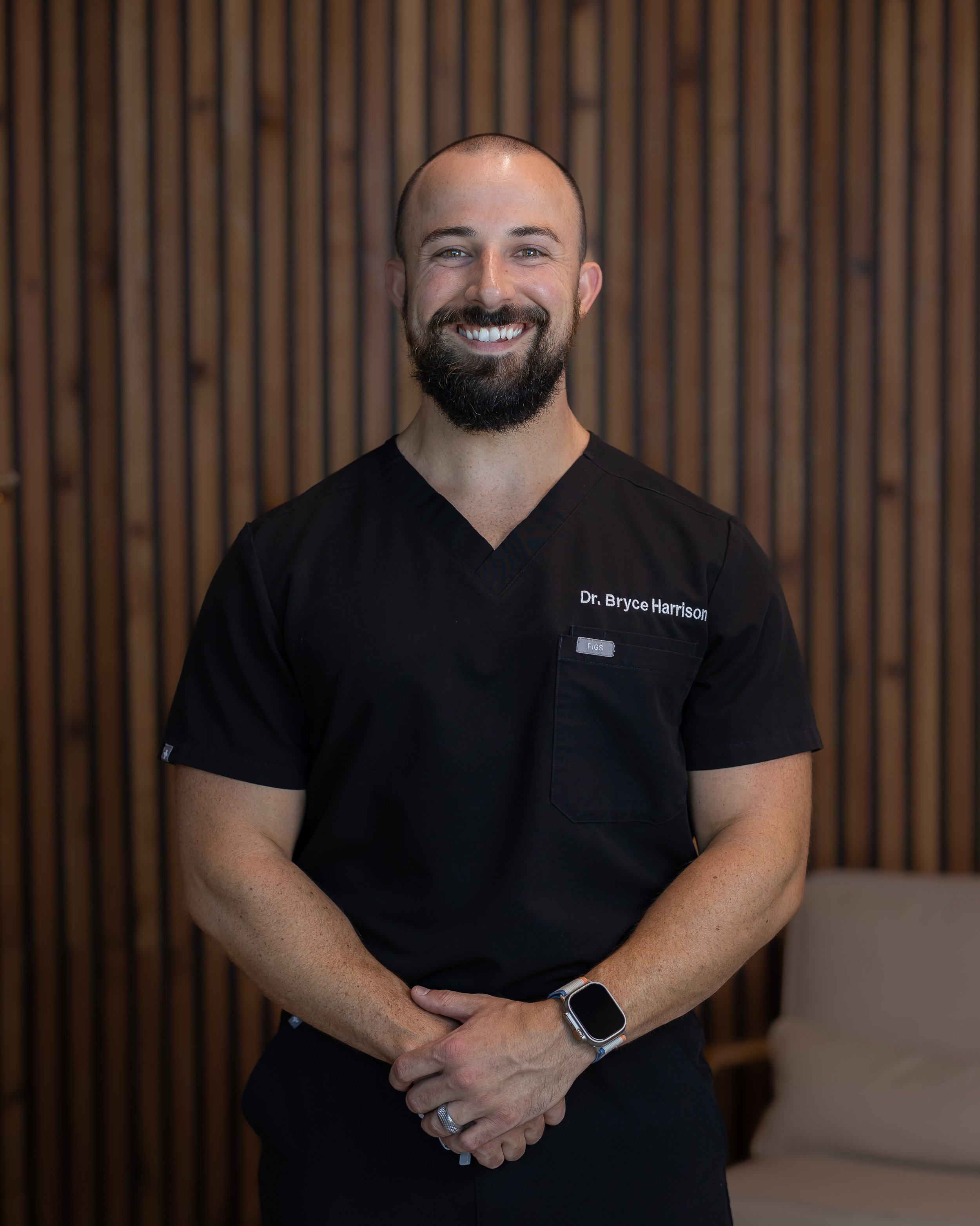 Dr. Bryce Harrison smiling at the camera standing in front of a wooden wall.