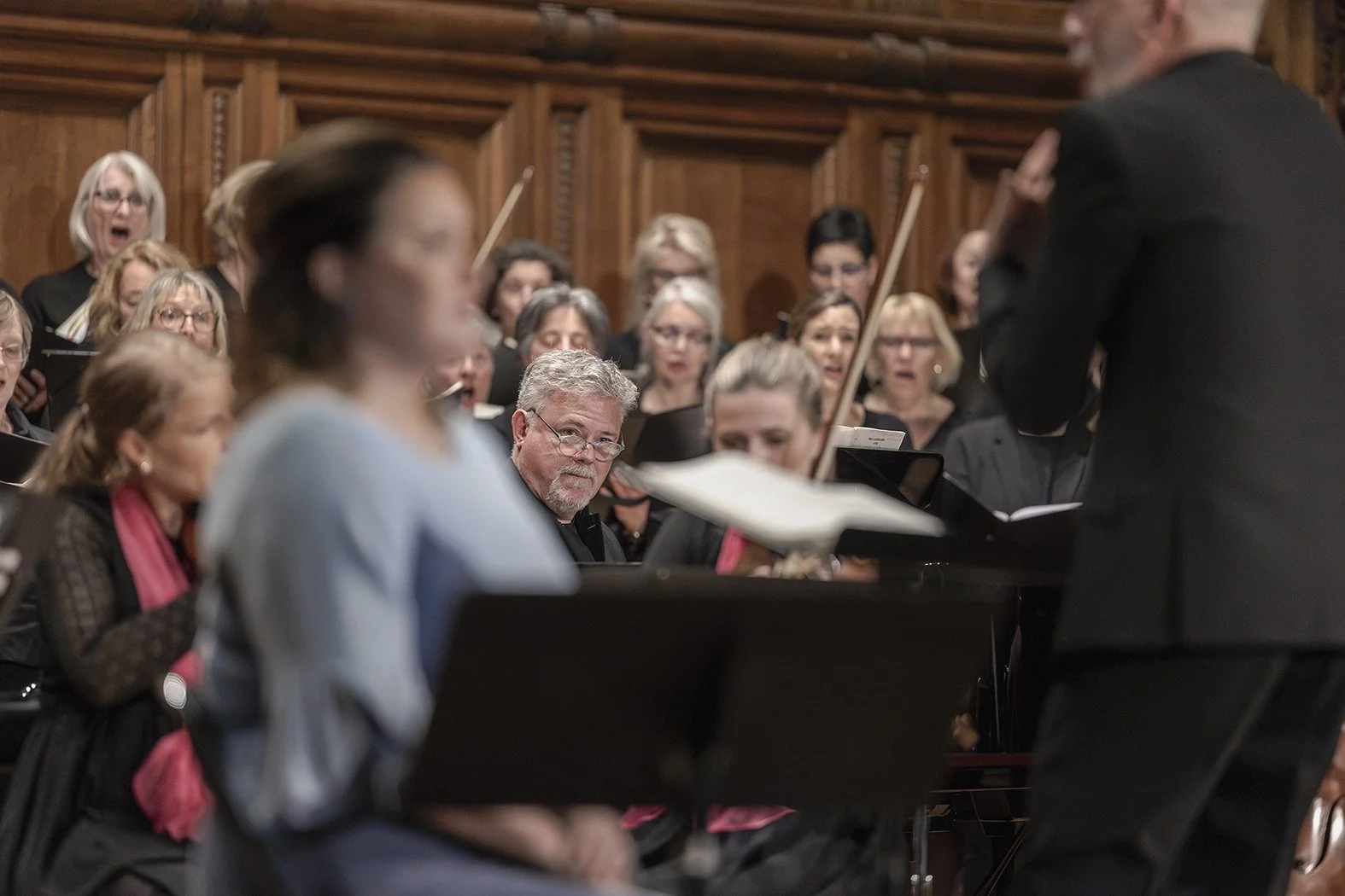 Orquesta sinfónica en actuación, con director y músicos en fondo de madera.