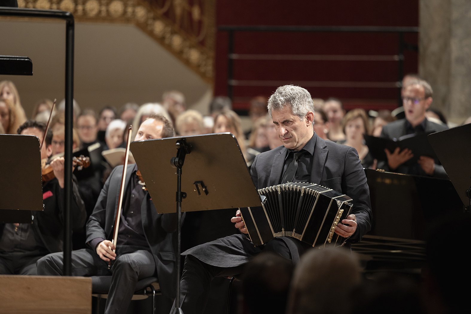 Un hombre tocando un acordeón en un concierto con una orquesta en un auditorio.