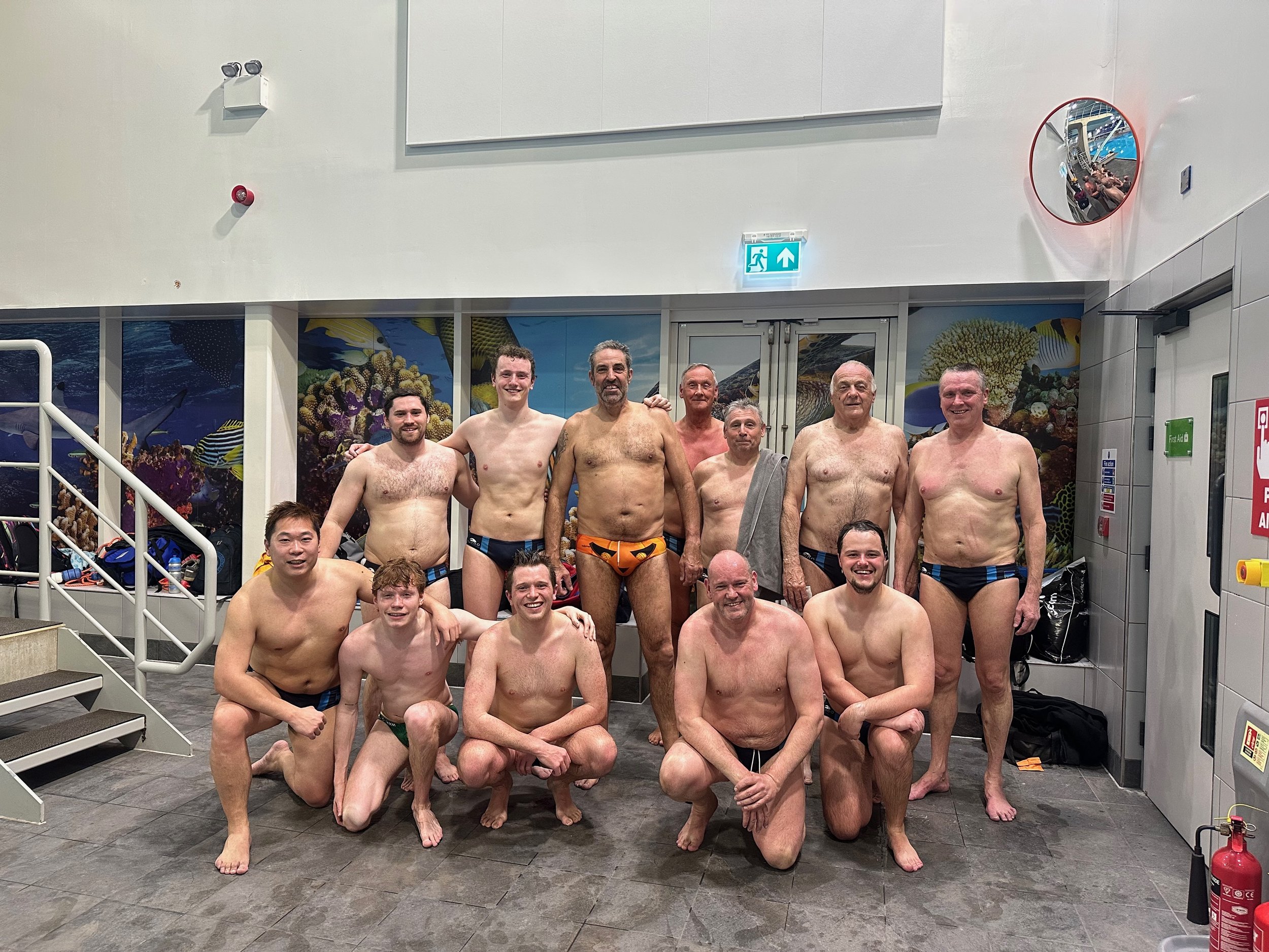 Group of men in swimwear posing for a photo at an indoor swimming pool.