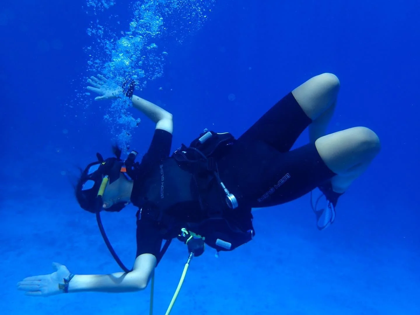 Person scuba diving underwater, wearing a diving mask, wetsuit, and oxygen tank, with one hand extended and opening palm.  Cozumel Scuba Diving Dive with k8