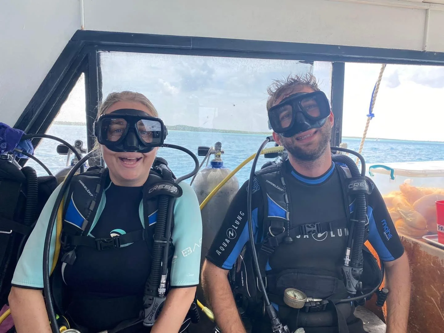Smiling man and woman in scuba diving gear, including masks, on a boat with water and sky in the background.  Cozumel Scuba Diving Dive with k8